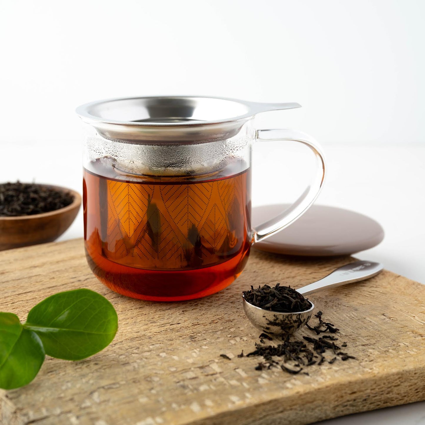 Earl Grey Français Black Tea shown as brewed tea in a clear mug next to a scoop and dish full of loose leaf tea.