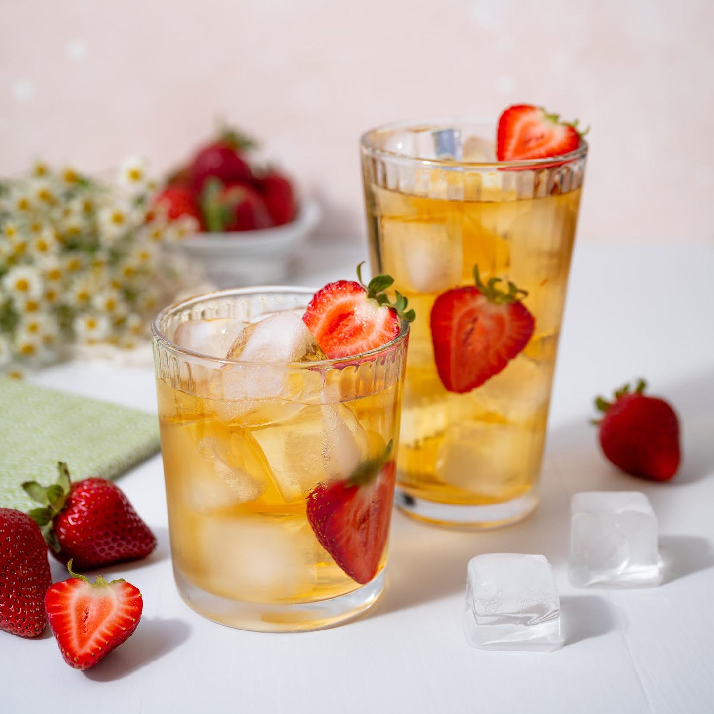 Summer Romance Black and Green Tea Blend shown brewed and iced in two clear cups with strawberries. In the background is a bowl of strawberries and a bundle of flowers.