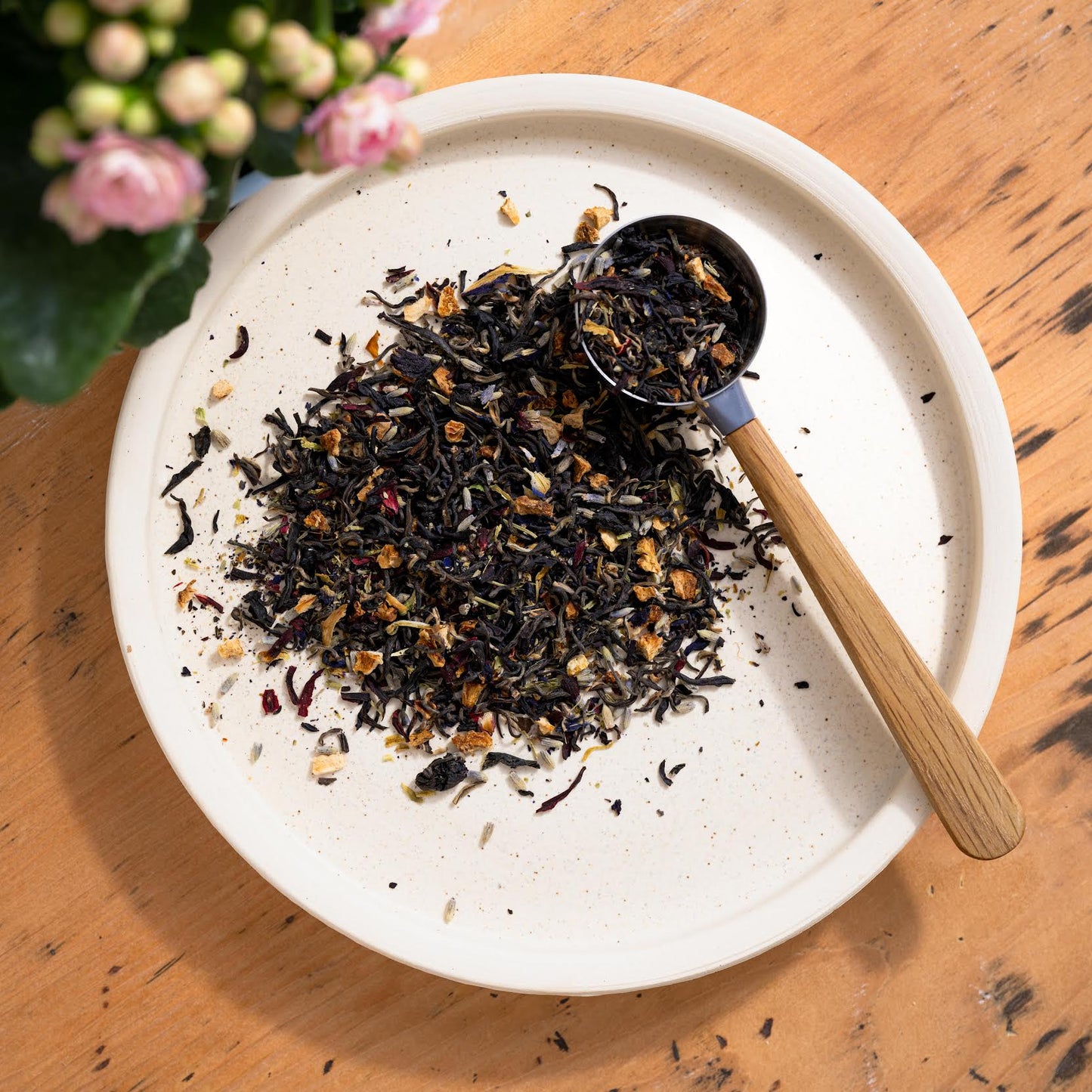 Miss Violet Purple Leaf Tea shown as loose leaf tea on a white dish as well as in a wooden handled tablespoon.