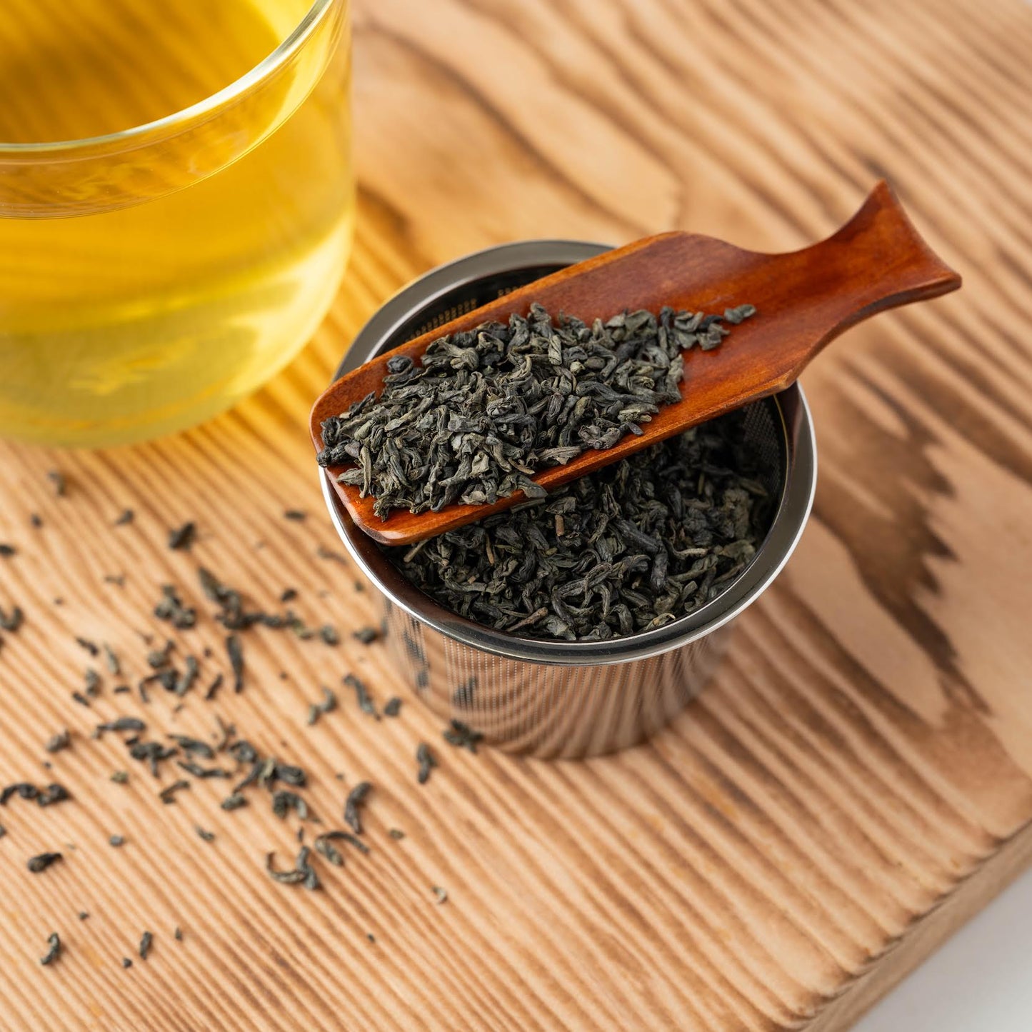 Chun Mee Green Tea shown as loose leaf tea in a wooden scoop and strainer with a clear cup of brewed tea nearby.