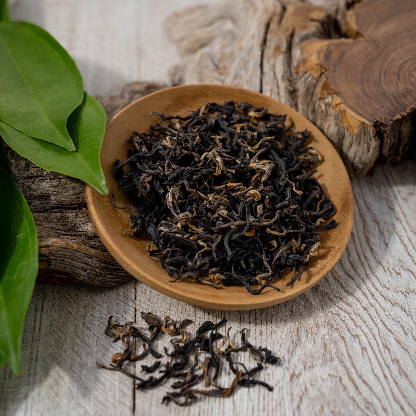 Kenyan Purple Leaf Tea shown as loose tea leaves in a wooden dish, on top of a piece of wood.