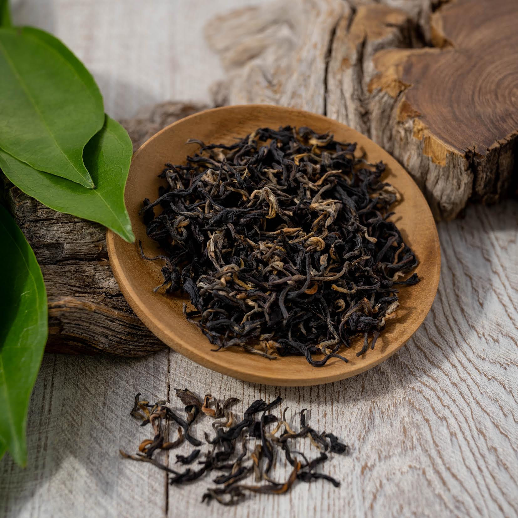 Kenyan Purple Leaf Tea shown as loose tea leaves in a wooden dish, on top of a piece of wood.