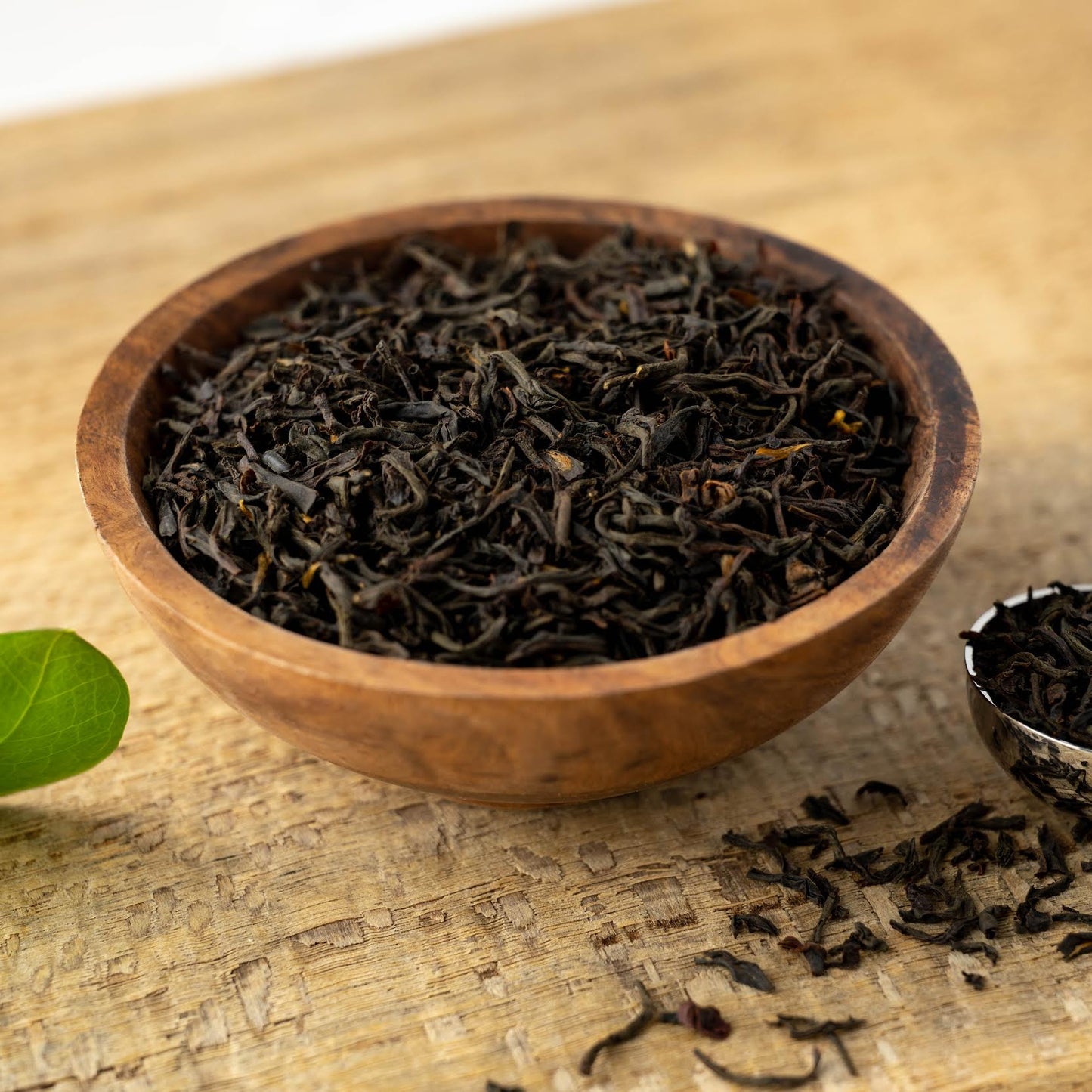 Earl Grey Français Black Tea shown in a wooden bowl with a silver scoop full of loose leaf tea next to it.