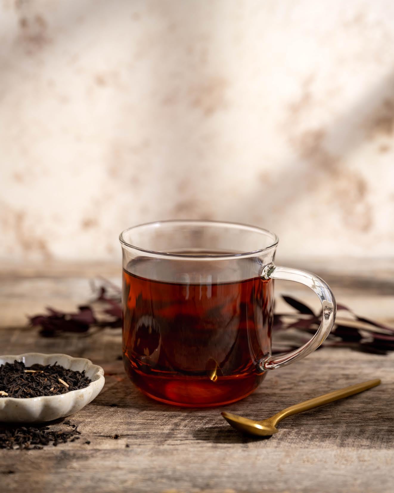 Caramel Pu-erh Tea shown as brewed tea in a clear mug with loose leaf tea in a dish next to it and a golden spoon.