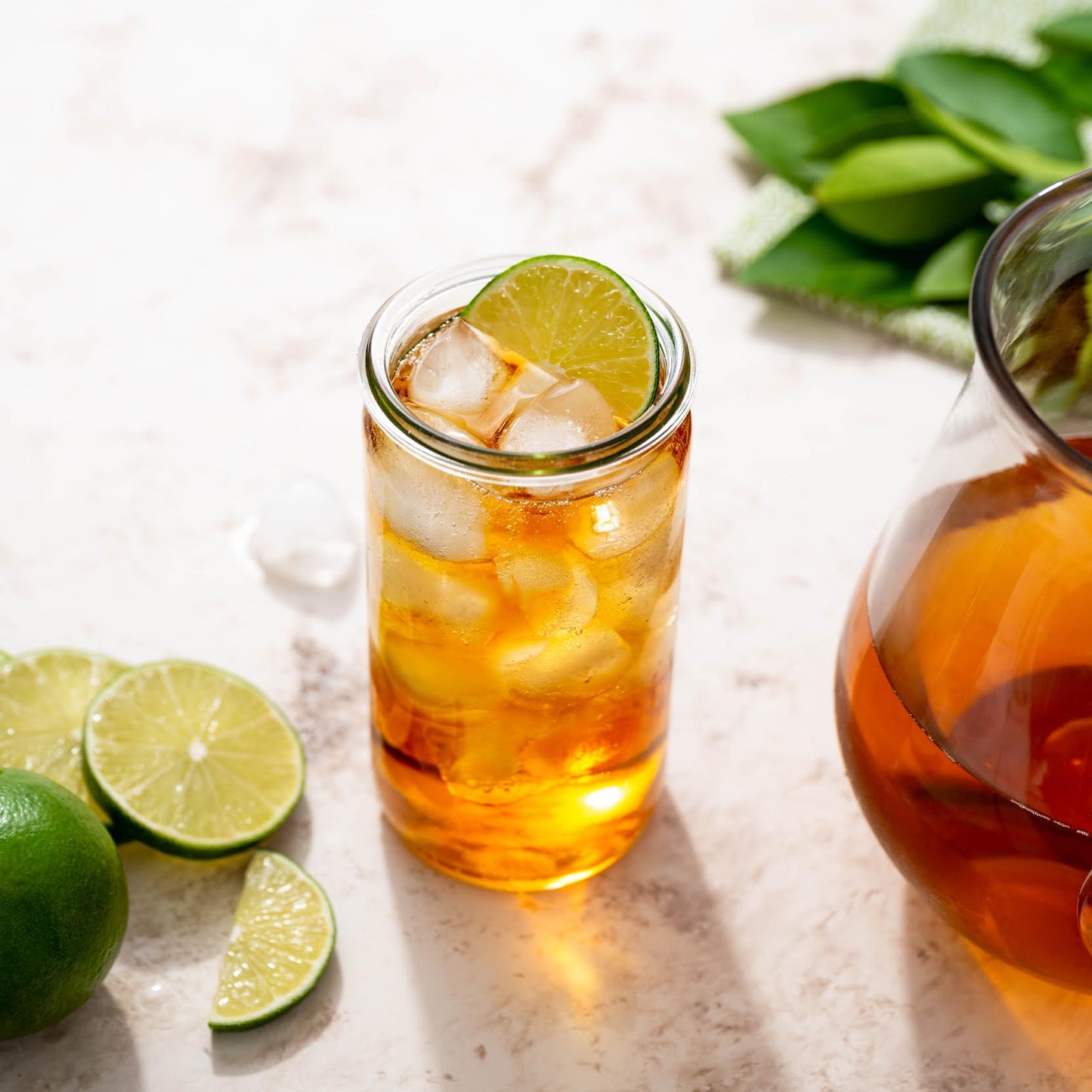 Nilgiri Black Tea show as iced tea with a slice of lime in a clear cup next to slices of lime and a container of brewed tea.
