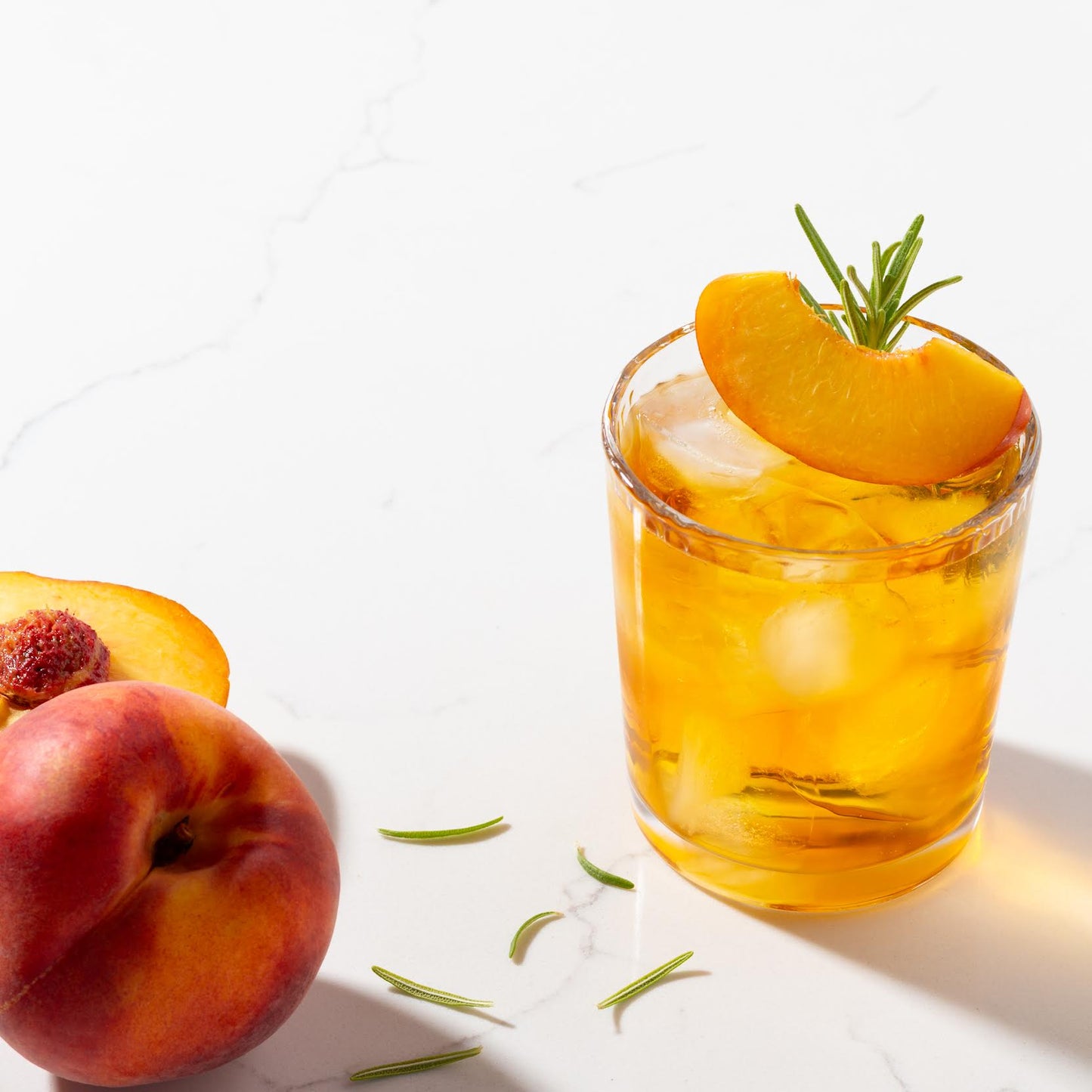 Peach Rooibos Herbal Tea shown as an ice tea garnished with a slice of peach and next to two peaches.