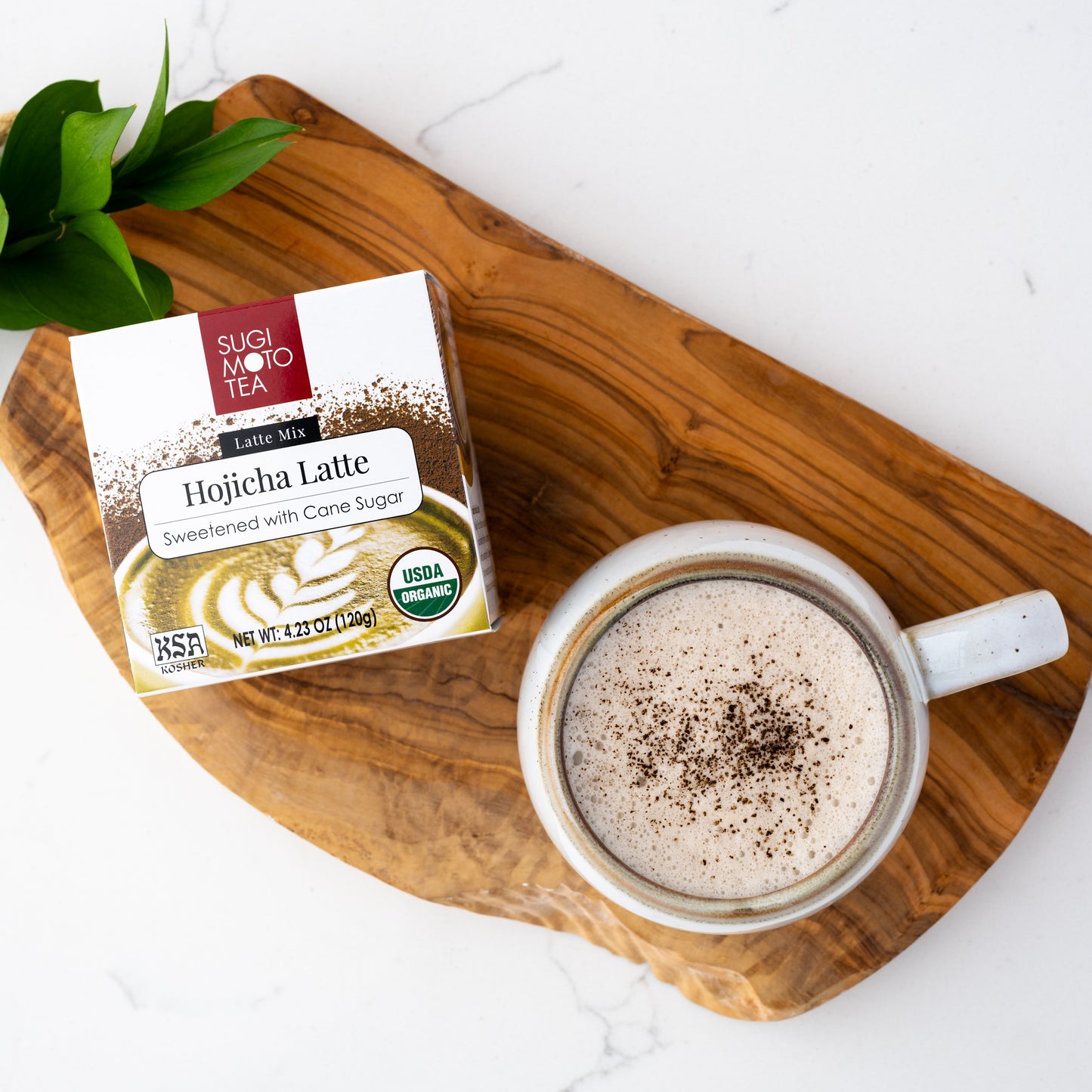 Hojicha Latte shown packaged in a box next to a mug of hot Hojicha Latte on a wooden plank.