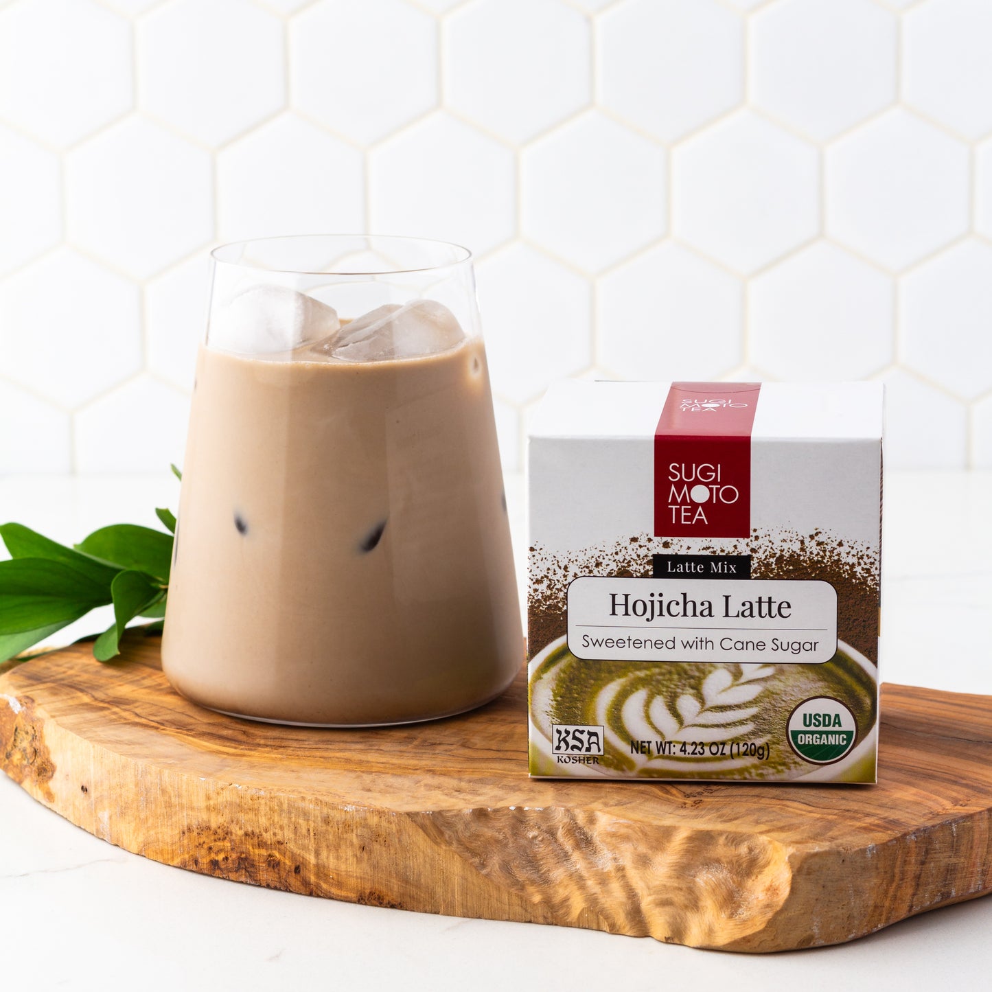 Hojicha Latte shown packaged in a box next to a cup of an iced Hojicha Latte on top of a wooden plank.