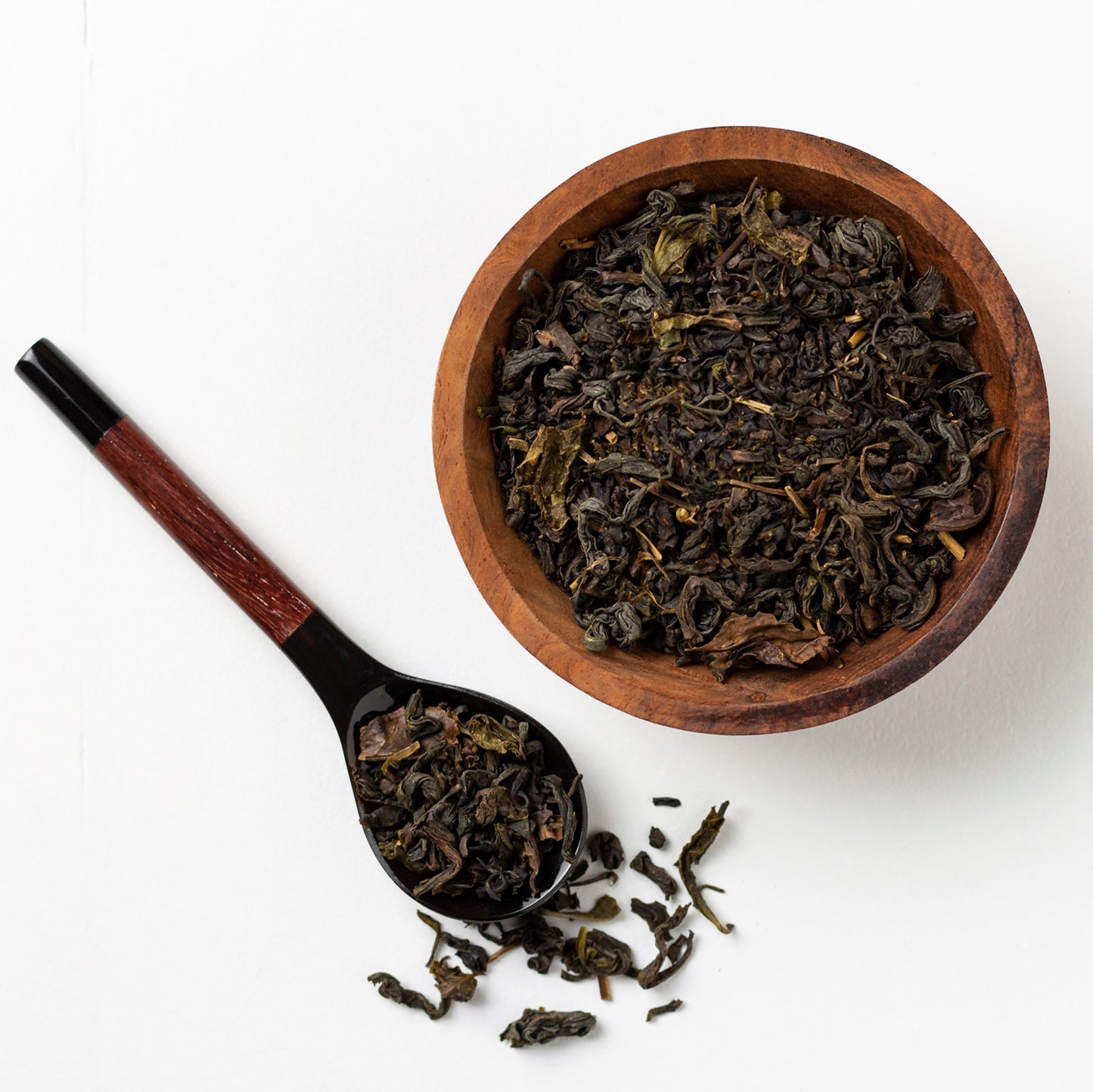 Japanese Oolong Tea shown from above as loose tea leaves in a small wooden bowl and spilling from a wooden spoon