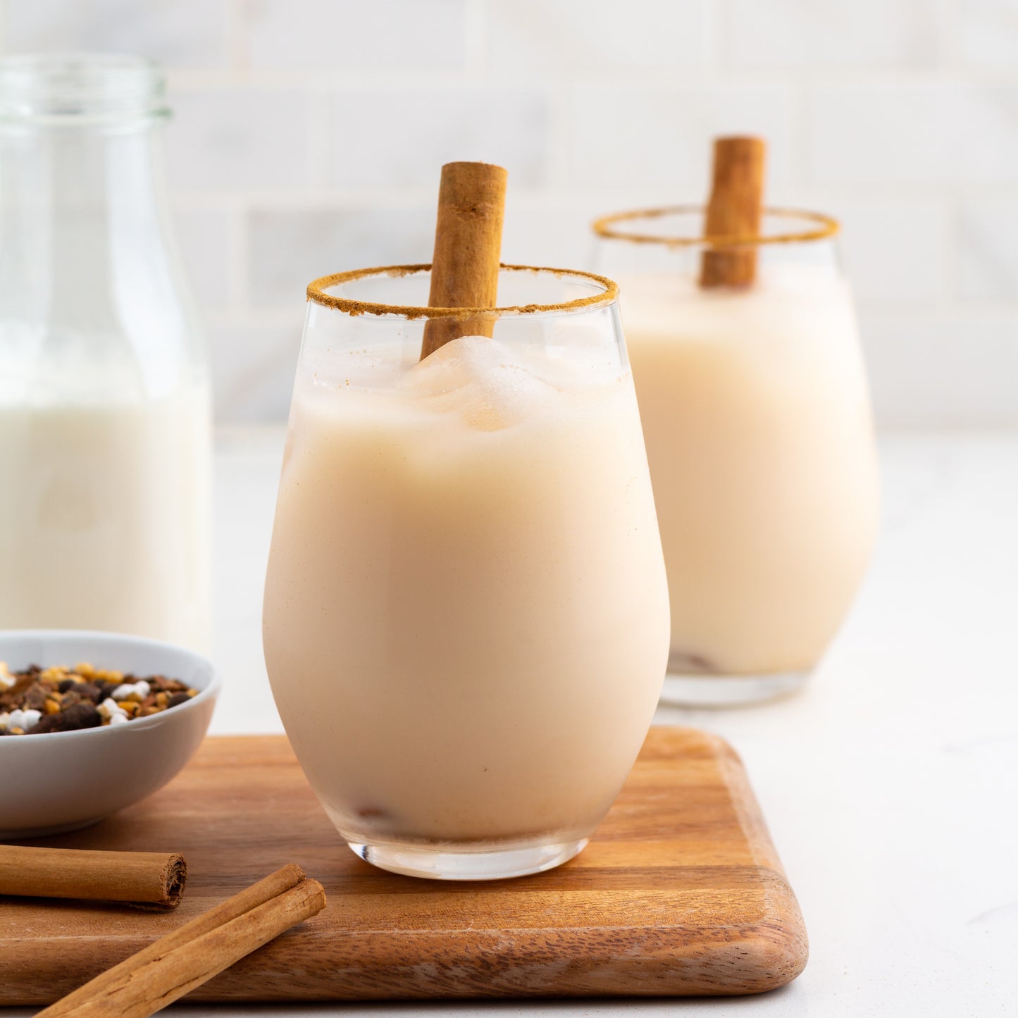 Horchata Rooibos Herbal Tea shown as milky iced tea in two glasses with cinnamon sticks and ground cinnamon on the rim of the glass.
