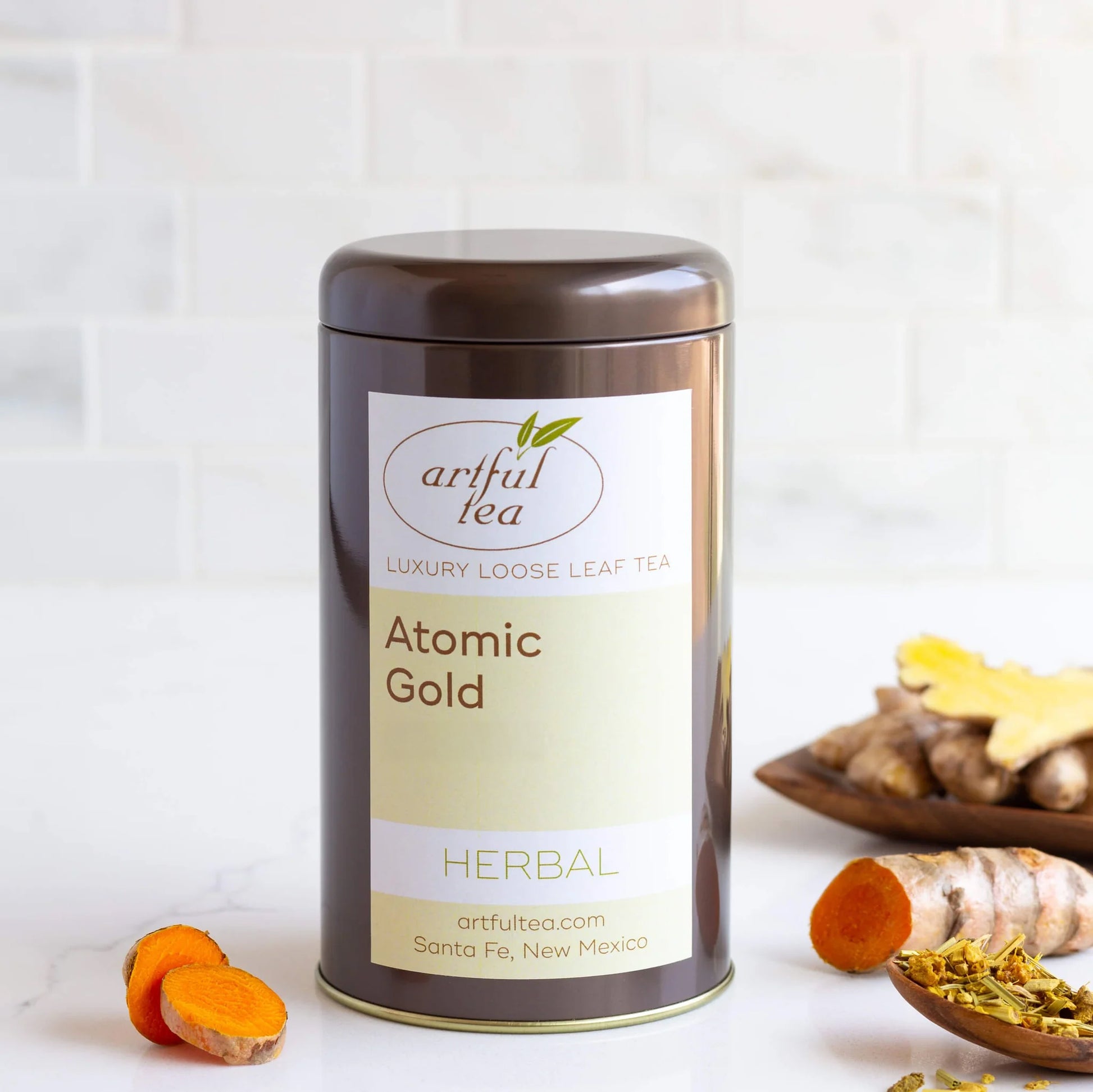 Atomic Gold Herbal Tea shown packaged in a brown tin surrounded by ingredients.