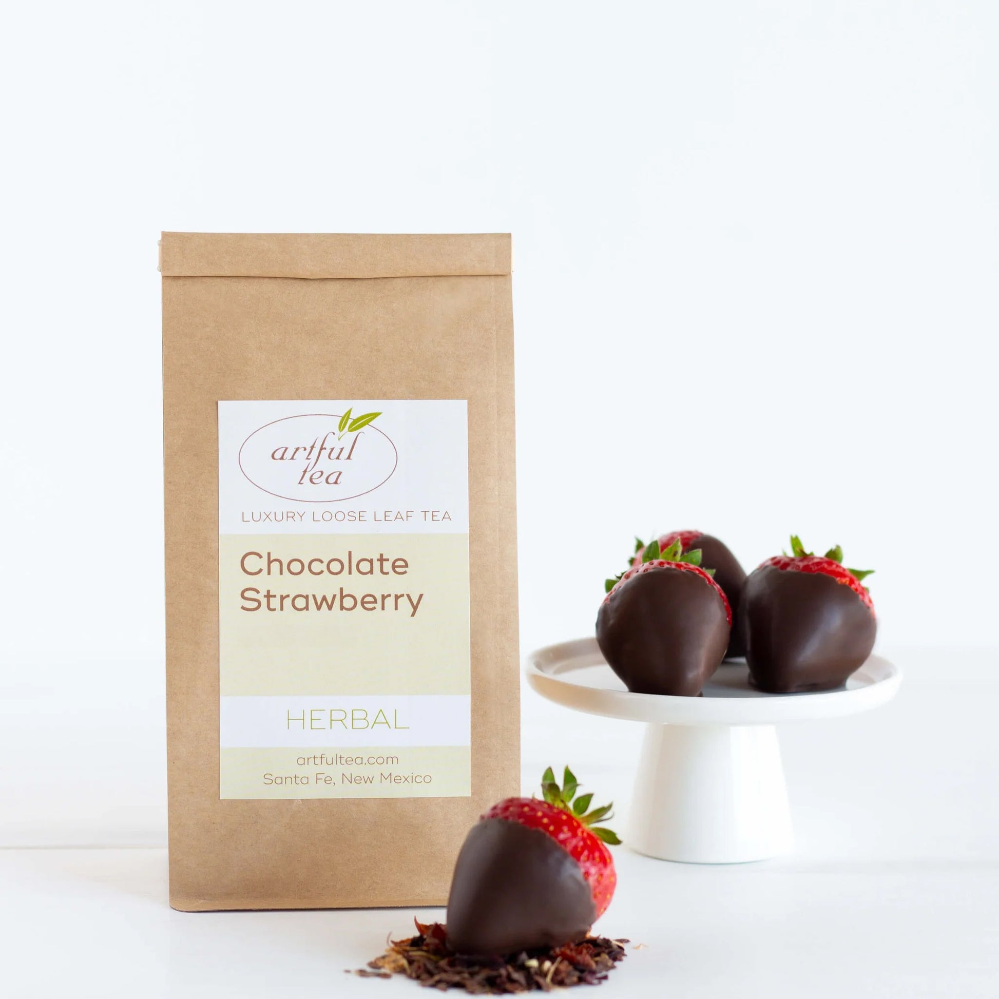Chocolate Strawberry Herbal Tea shown packaged in a brown Kraft bag next to a platter of chocolate covered strawberries.