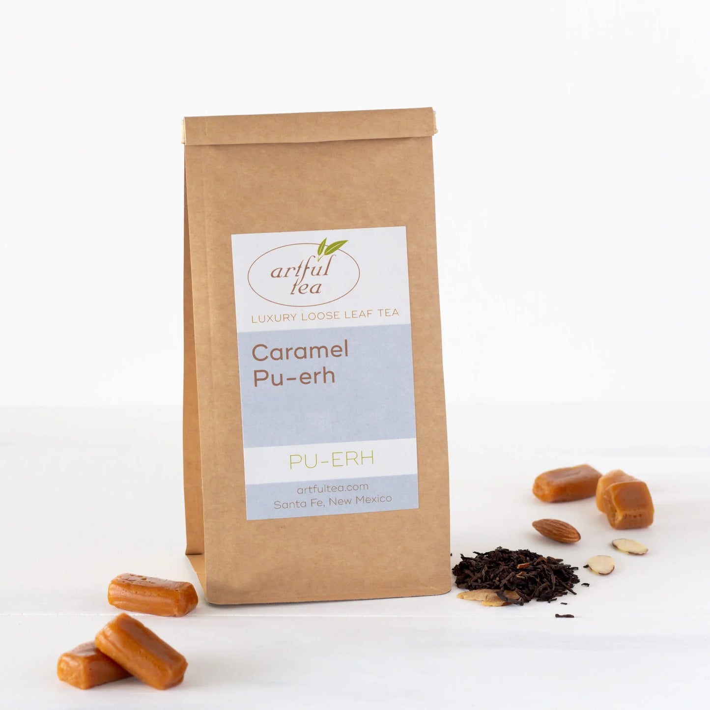 Caramel Pu-erh Tea shown packaged in a brown Kraft bag with lose tea leaves, almonds, and caramel next to it.