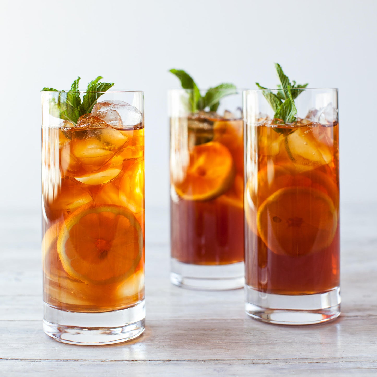 Apricot Brandy Black Tea shown as three cups of iced tea with mint sprigs and orange slices.
