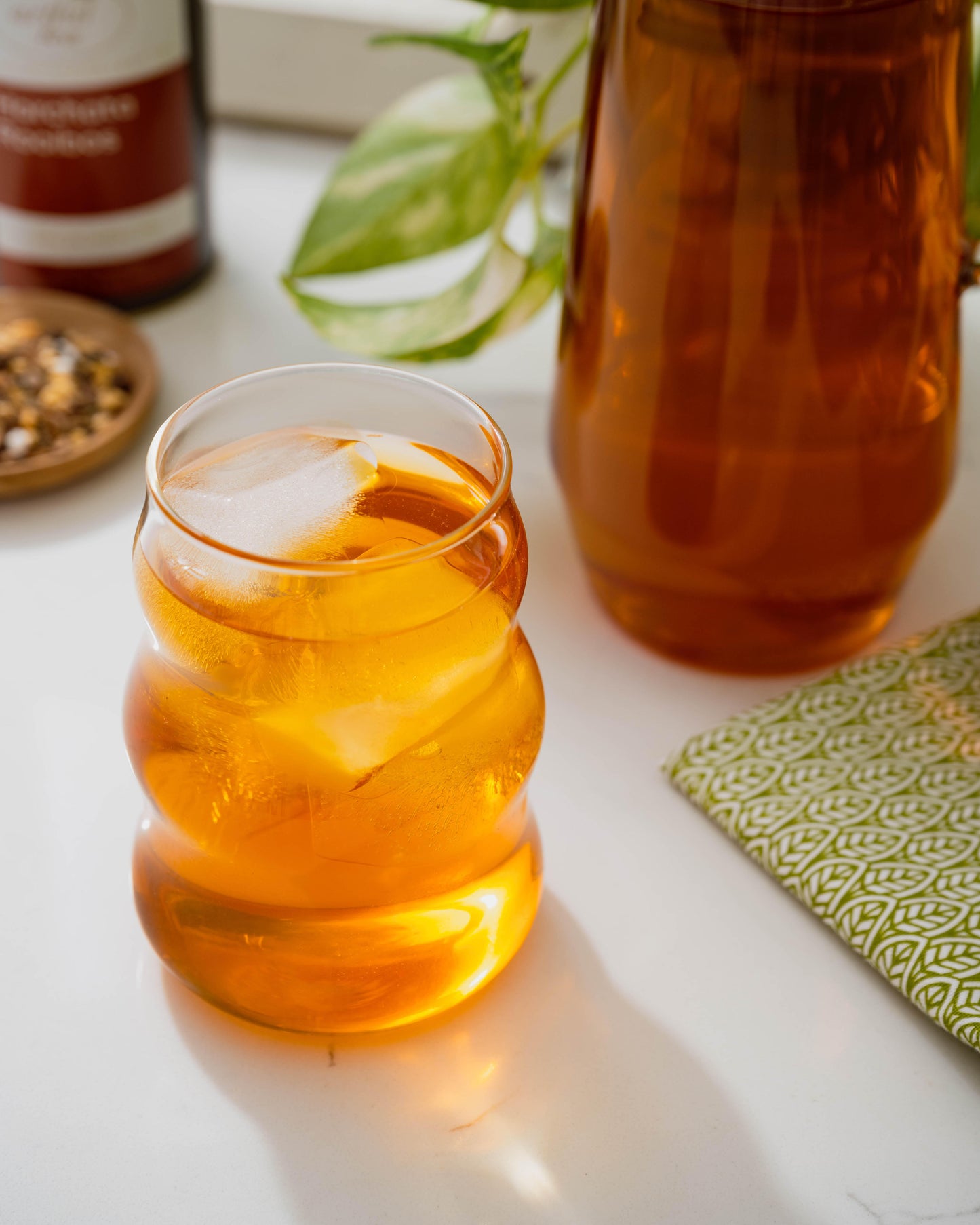 Horchata Rooibos Tea shown brewed in a clear cup with a large clear pitcher of brewed tea in the background.