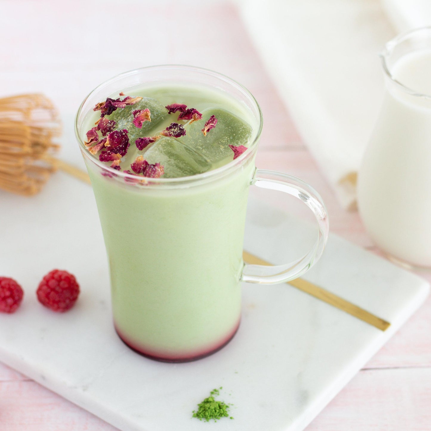 Culinary Grade Matcha as an iced raspberry, matcha latte in a clear mug on a marble tray with ingredients nearby.