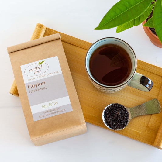 Organic Ceylon Black Tea shown packaged in a kraft bag on a wooden tray with a mug and scoop of loose tea