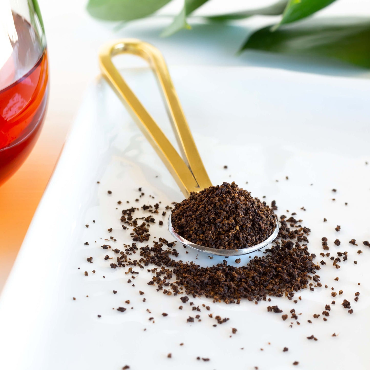 Irish Breakfast loose tea leaves shown on a golden spoon with tea leaves spilling out on a white platter.