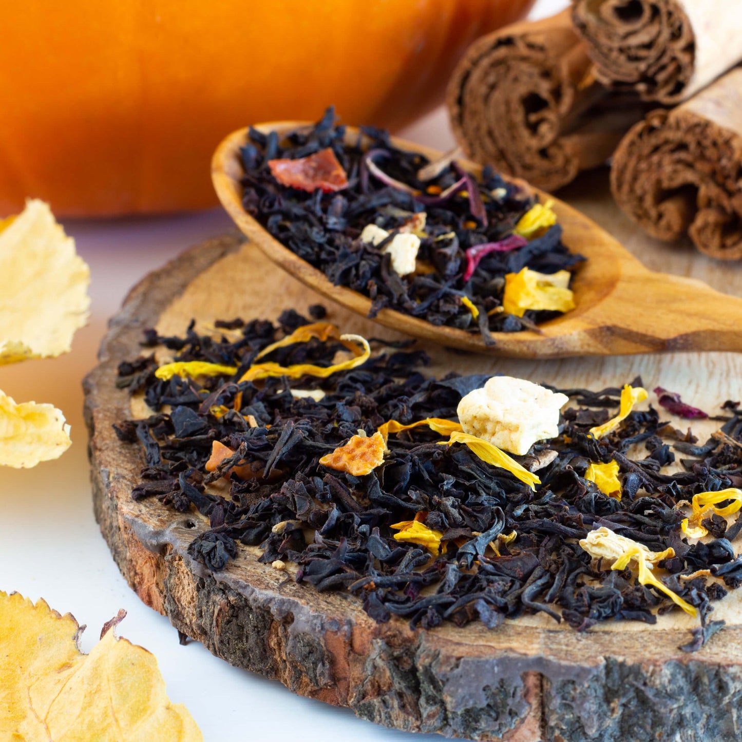 Fall Fiesta loose tea leaves shown on top of a wooden coaster and in a wooden scoop with cinnamon sticks and a pumpkin in the background.