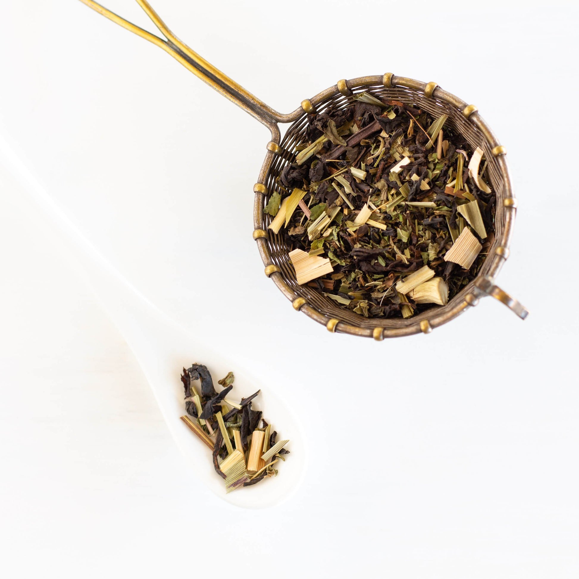 Lemon Mint Ménage loose black tea leaves in a golden spoon with a smaller white spoon next to it.