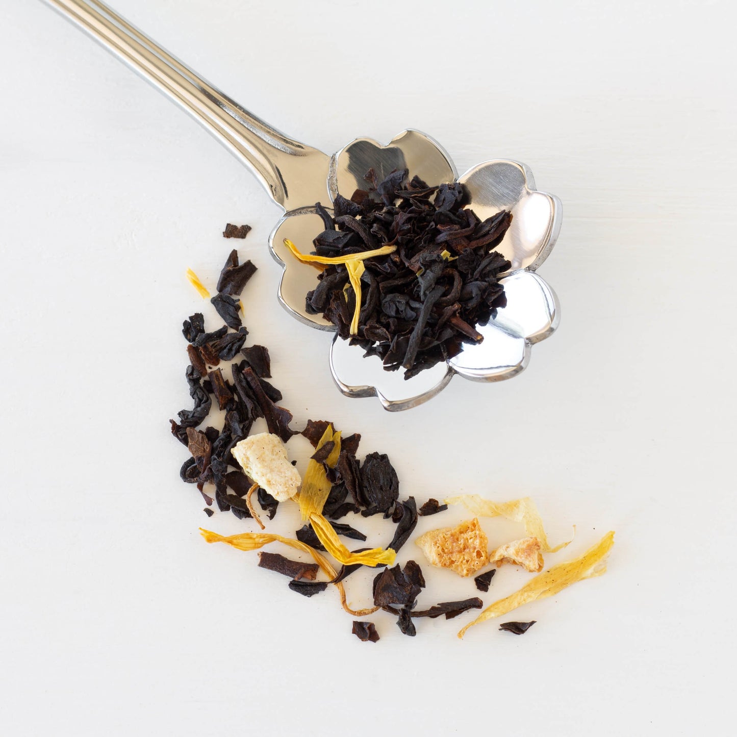 Pomegranate Lemon loose black tea leaves on a silver, flower spoon with more loose tea next to it.