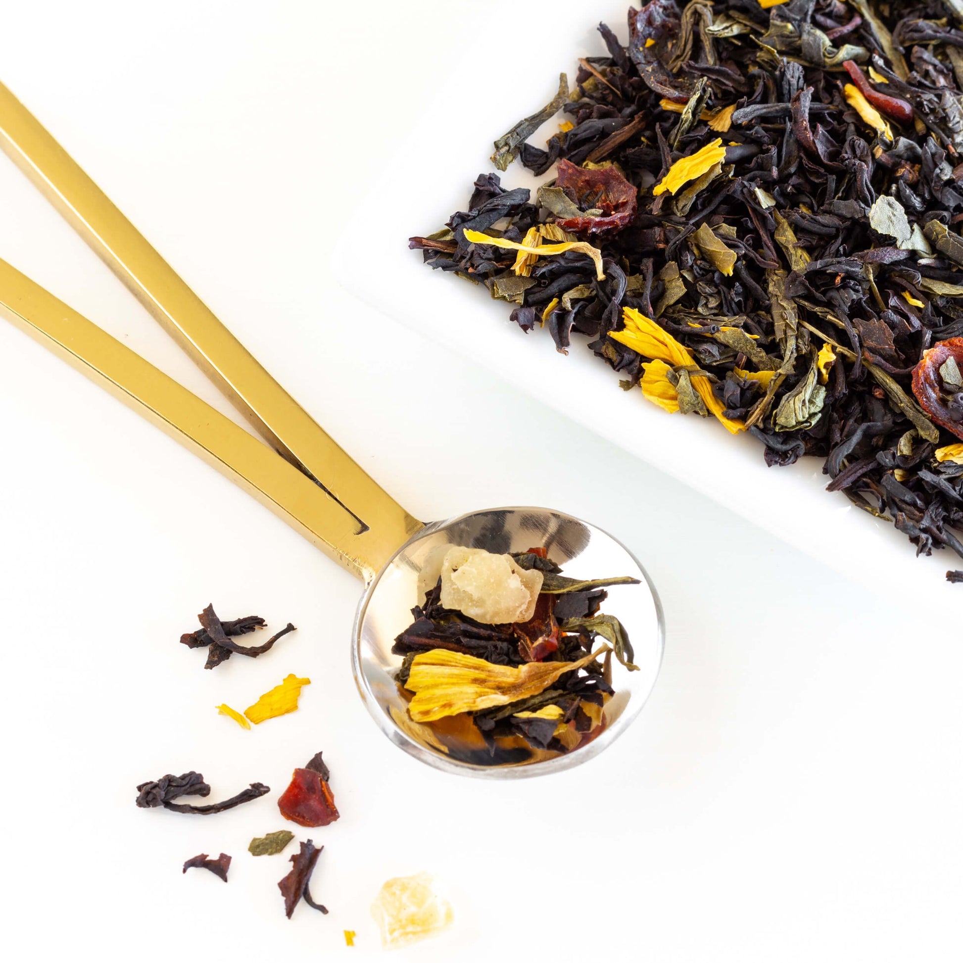 Summer Romance Black and Green Tea loose leaves shown in a gold spoon next to a square pile of loose tea leaves.