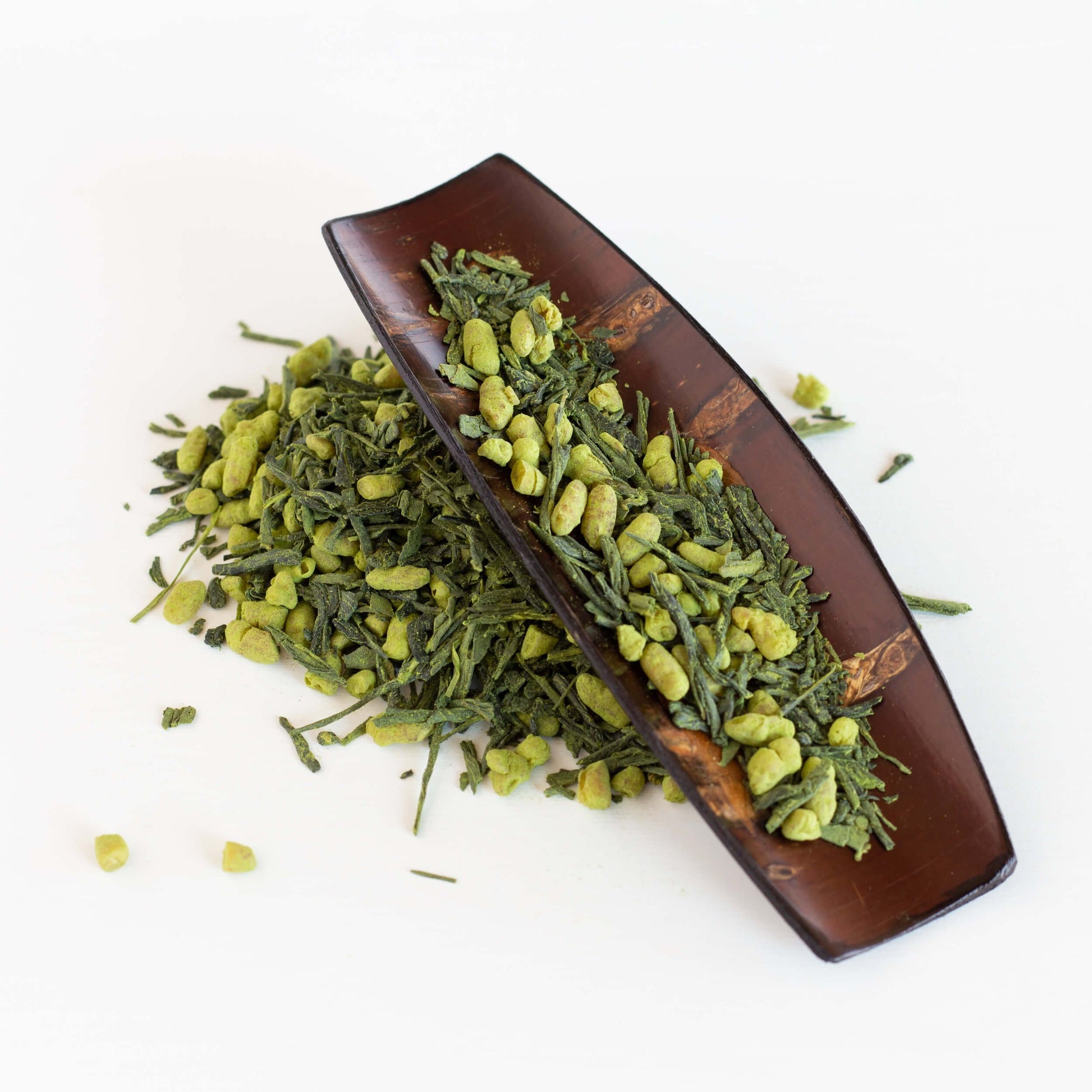 Genmaicha Matcha Green Tea shown as loose leaf tea spilling out of a cherry wood scoop.