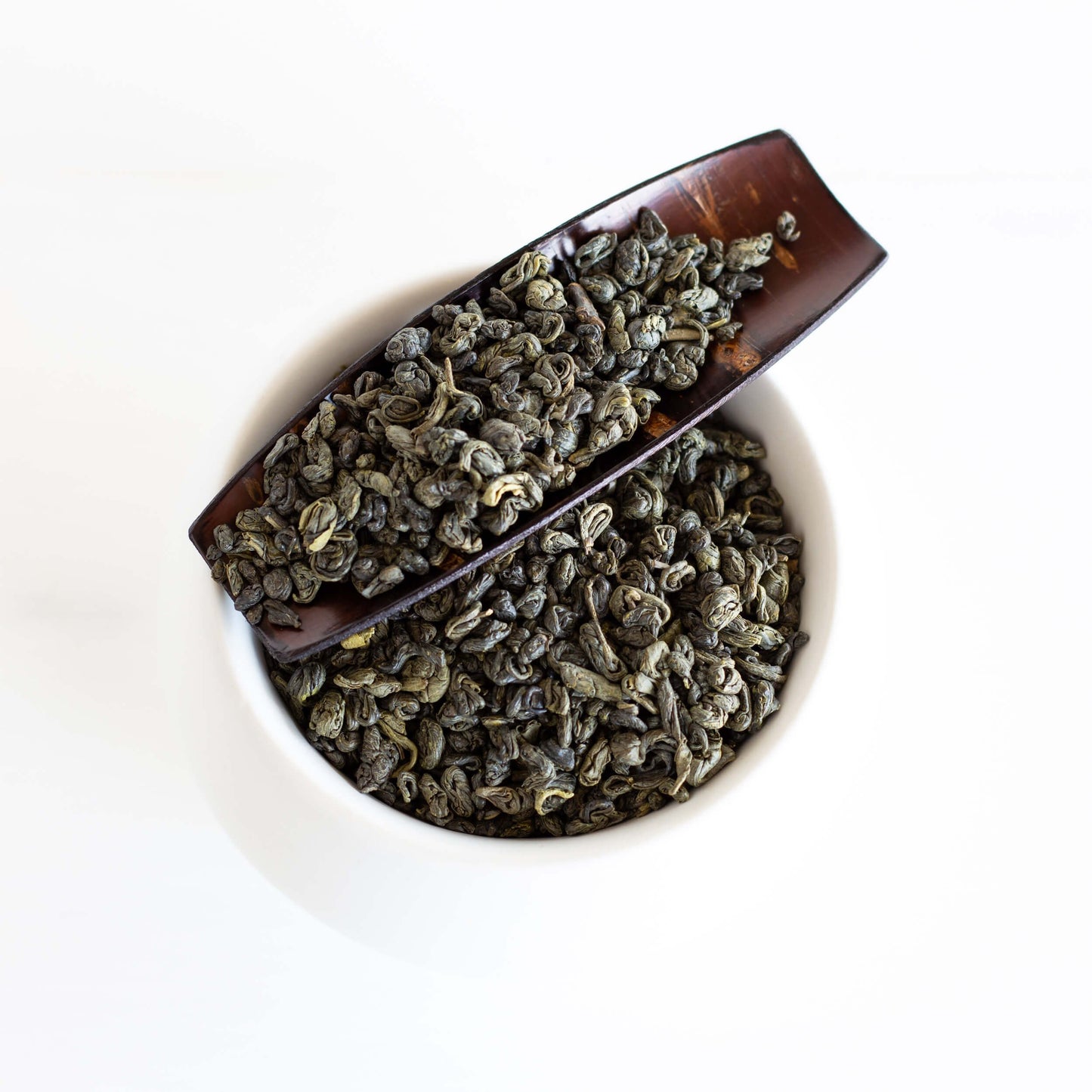 Gunpowder Green Tea shown as loose leaf tea on a brown platter in a white dish.