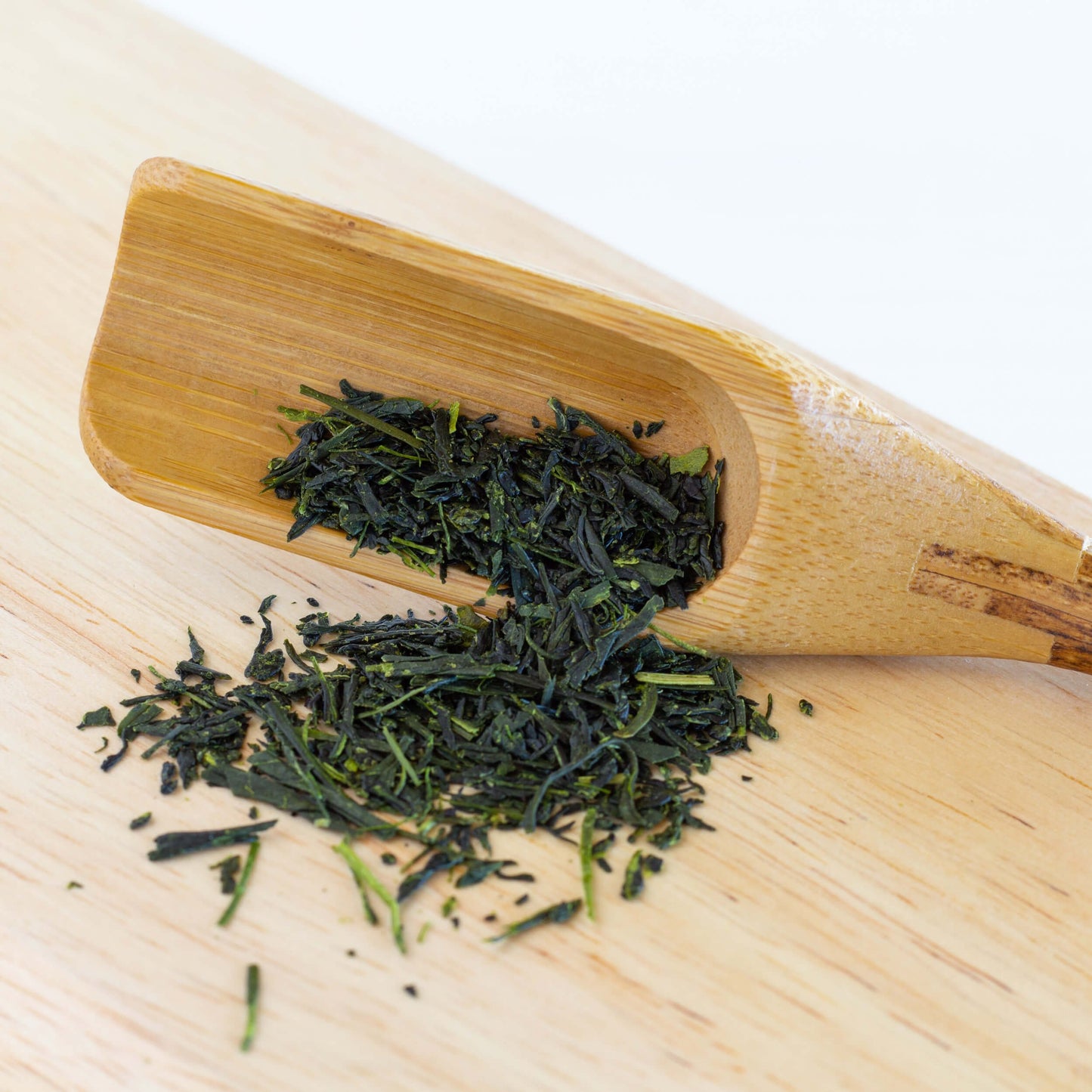 Gyokuro Green Tea shown as loose leaf tea spilling out of a wooden scoop onto a bamboo plank.