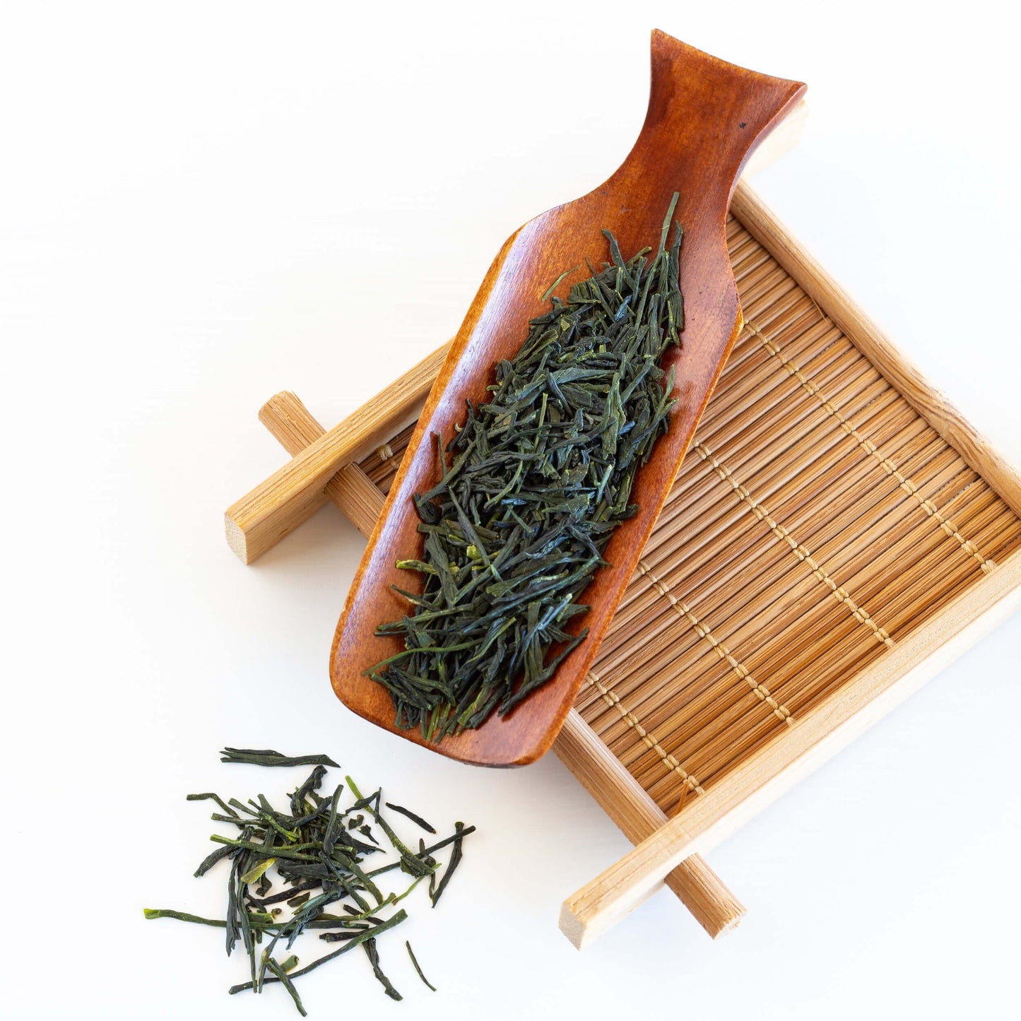 Kabusecha Green Tea shown as loose leaf tea in a wooden scoop on top of a bamboo coaster.