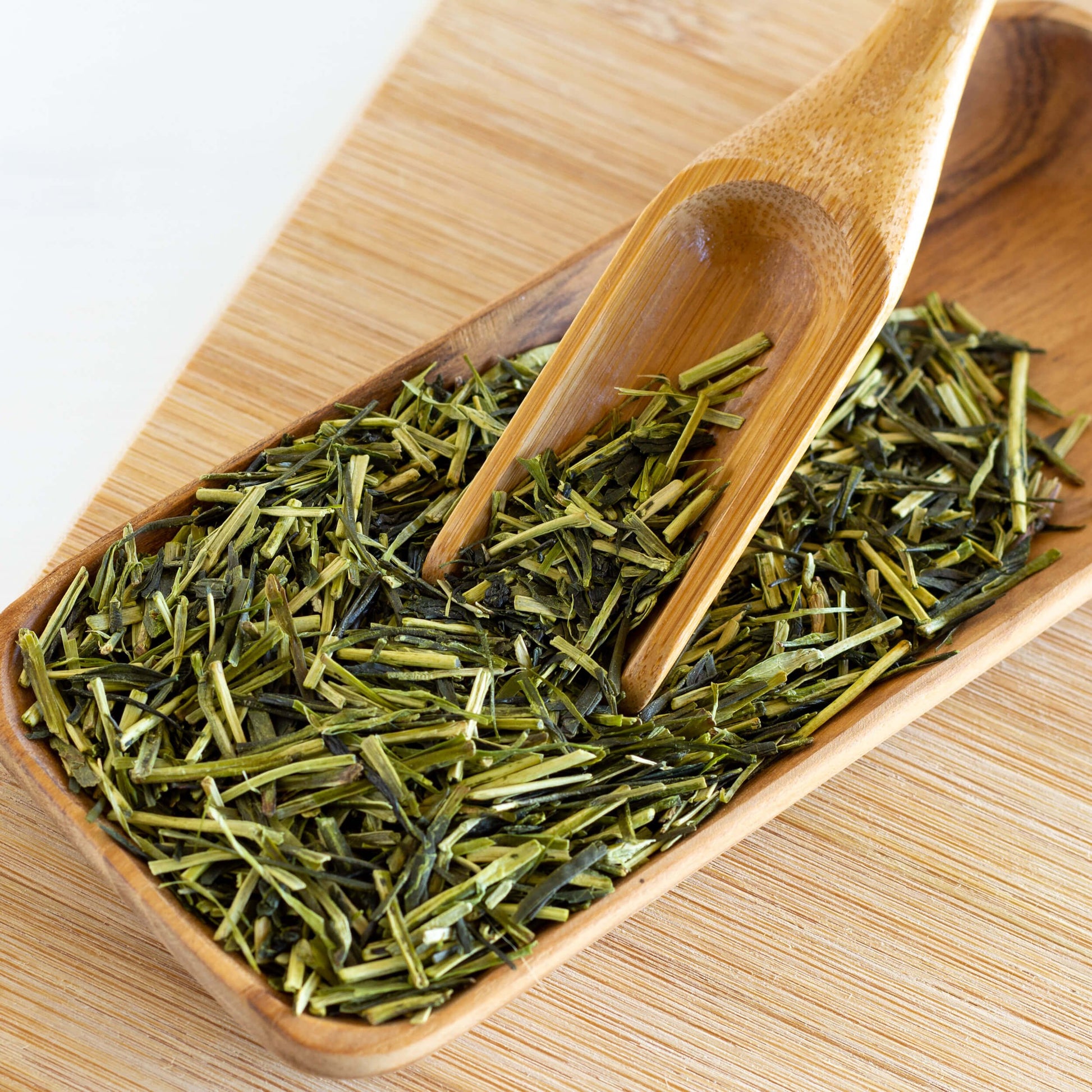 Kukicha Green Tea shown as a loose leaf tea spilling out of a wooden scoop into a wooden tray.