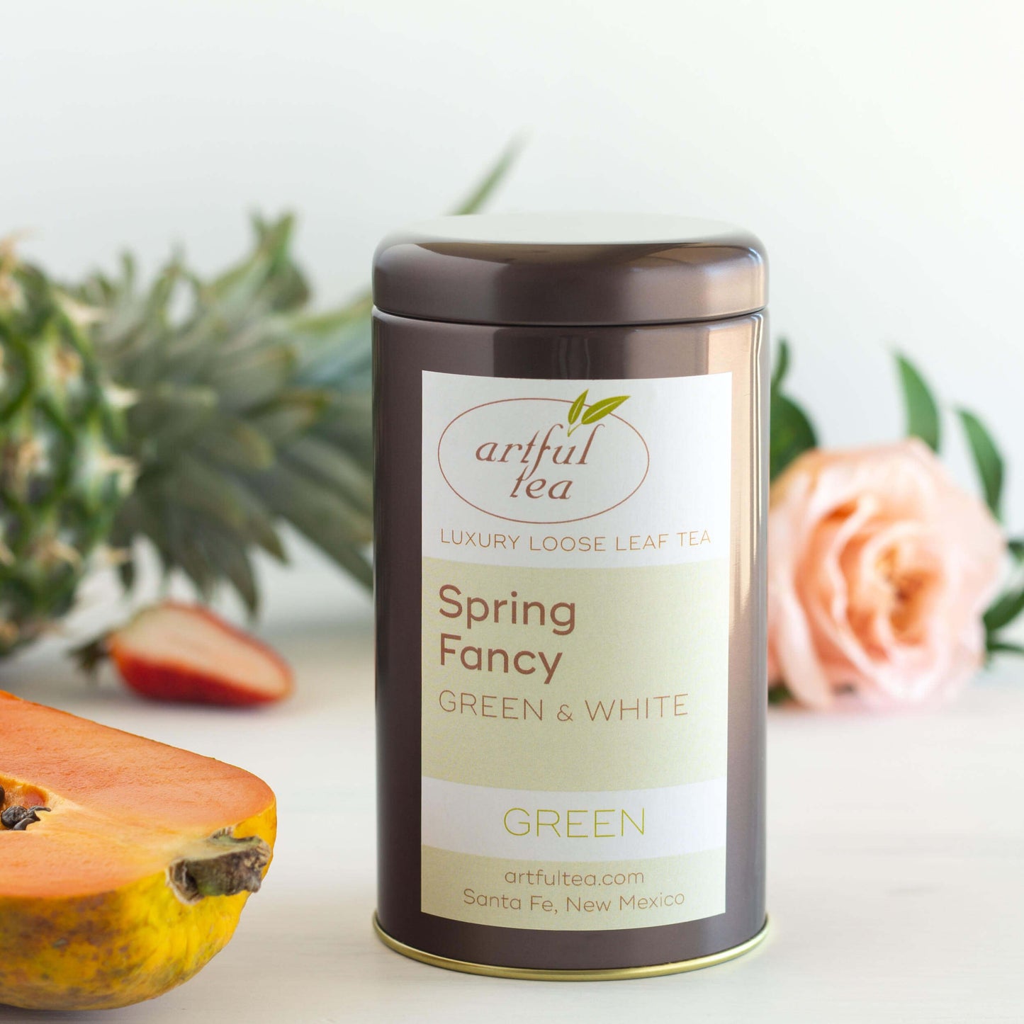 Spring Fancy Green and White Tea shown packaged in a brown tin surrounded by ingredients and a pink rose.