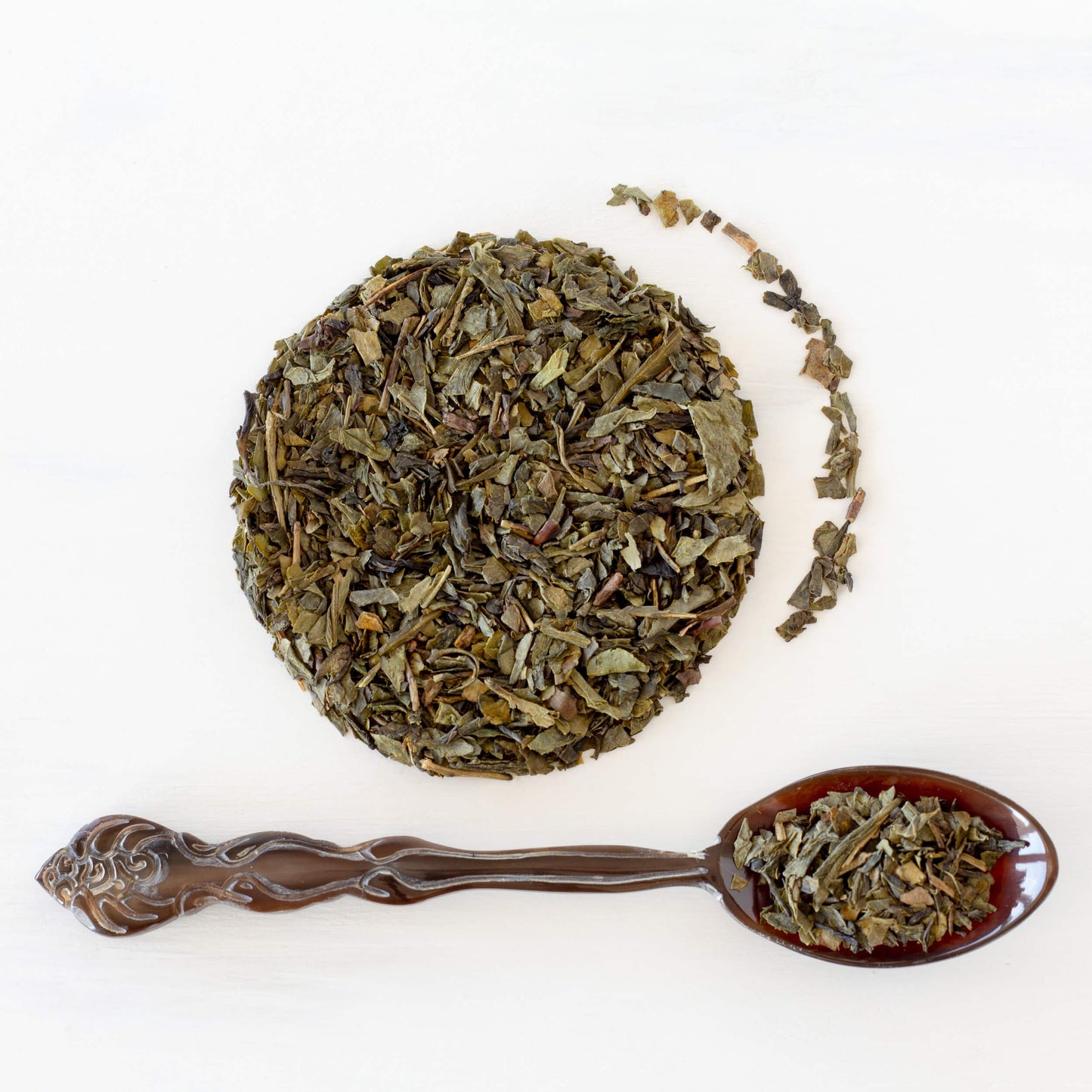 Vanilla Bean Green Tea shown from above as loose leaf tea in a circle with a spoon full of tea leaves in front of it and a bit of tea leaves beside it.