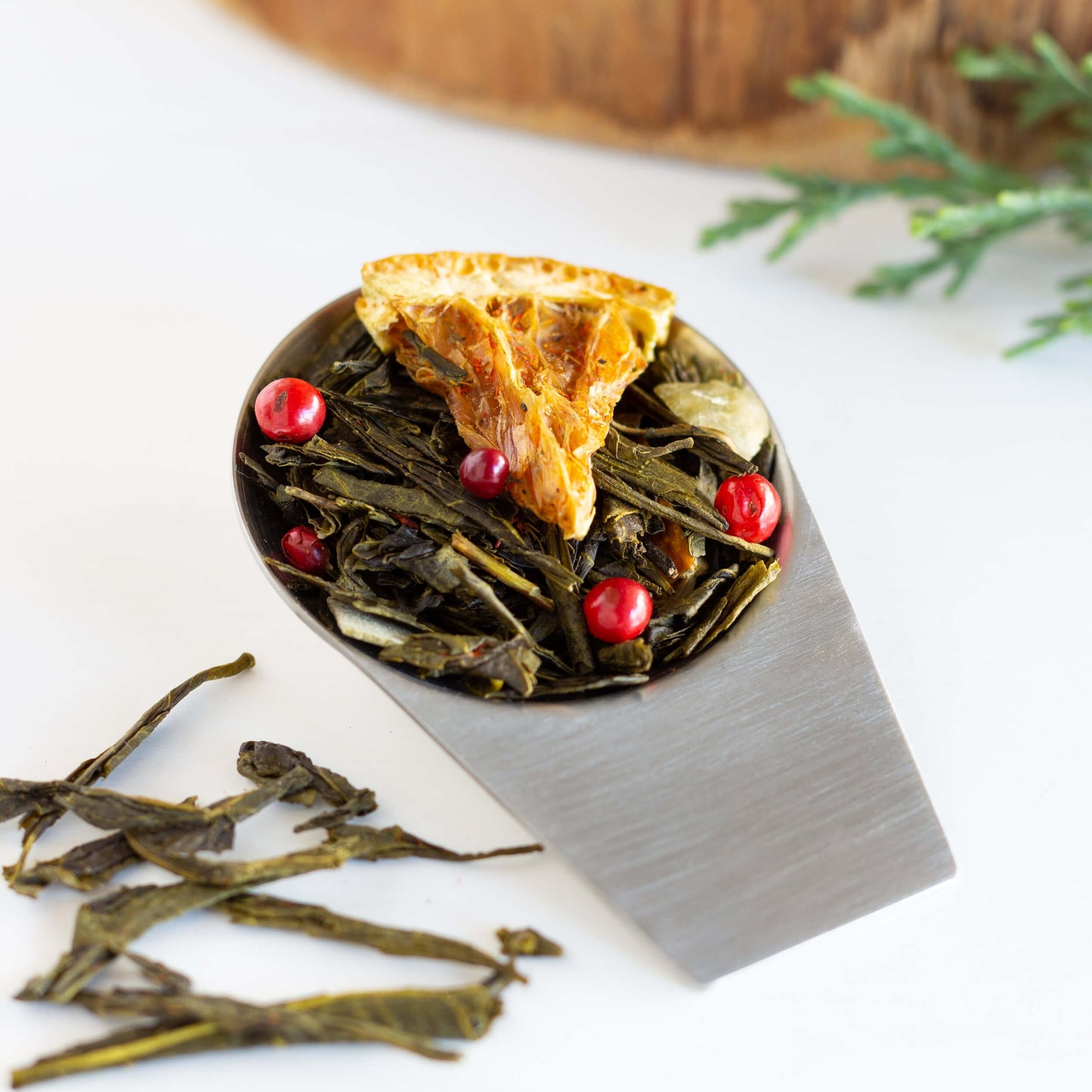 Winter Forest Green Tea shown as loose leaf tea in a silver scoop with tea leaves strewn on the side.