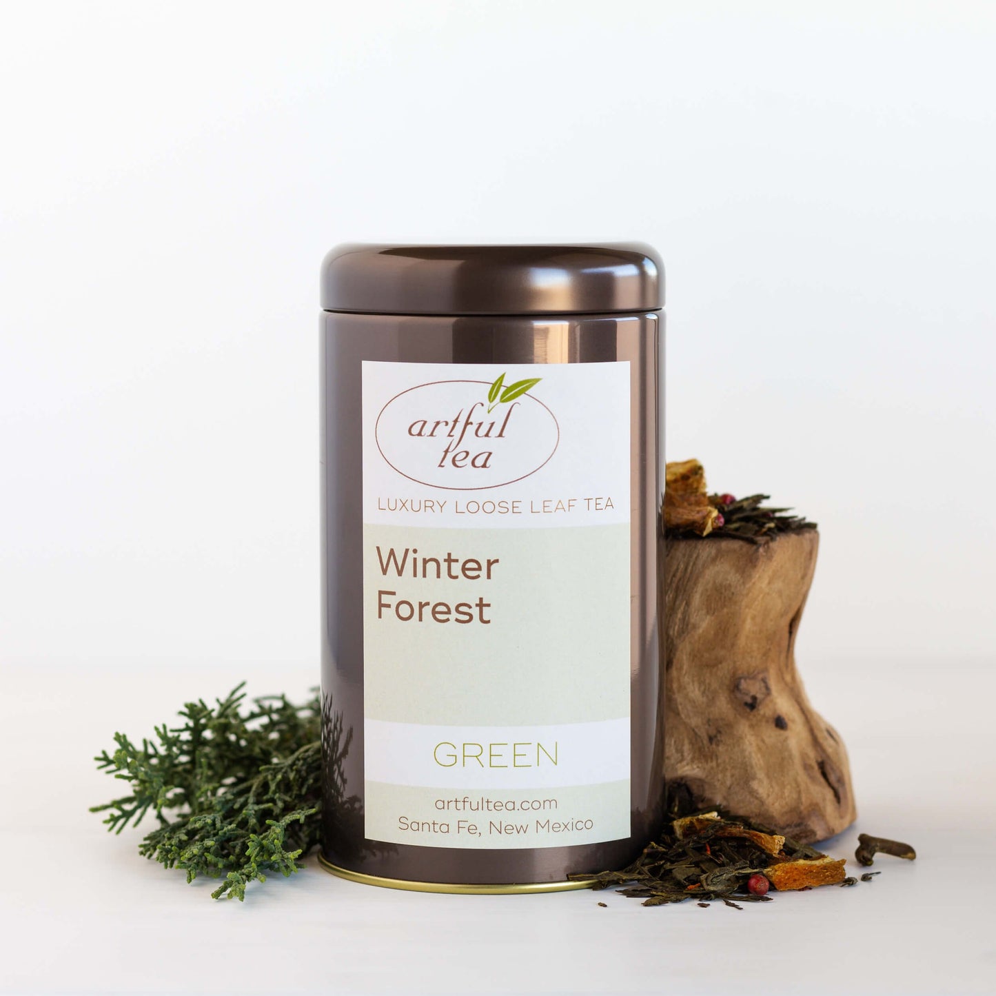 Winter Forest Green Tea shown packaged in a brown tin with ingredients nearby.