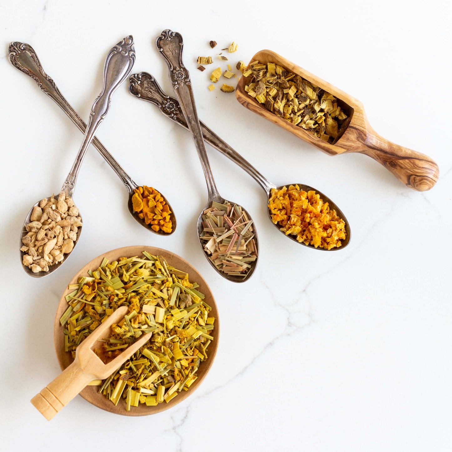 Atomic Gold Herbal Tea shown from above as loose leaf tea in a wooden bowl next to spoons full of different ingredients.