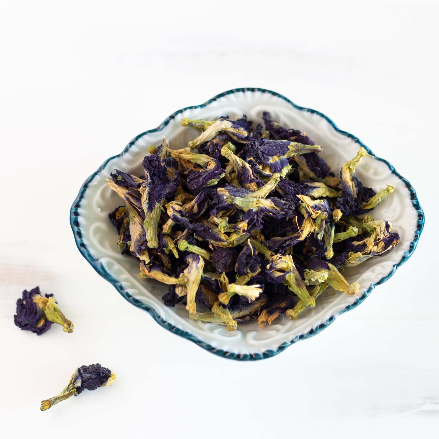 Butterfly Pea Flower Herbal Tea shown as loose leaf tea in a white bowl with a blue rim.