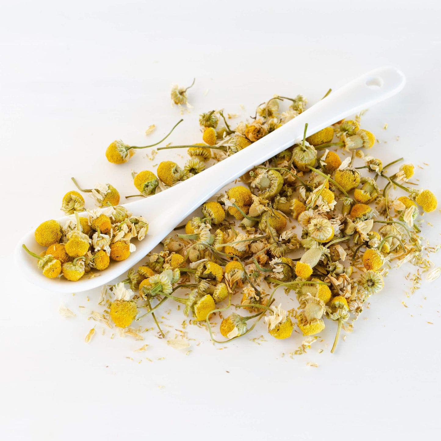 Egyptian Chamomile Herbal Tea shown as loose leave tea in a a white spoon on a pile of loose tea.