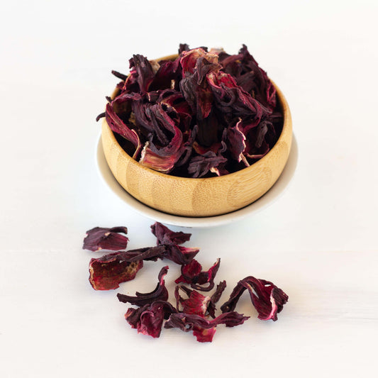 Hibiscus Herbal Tea shown as loose leaf tea in a wooden bowl with loose tea around it.