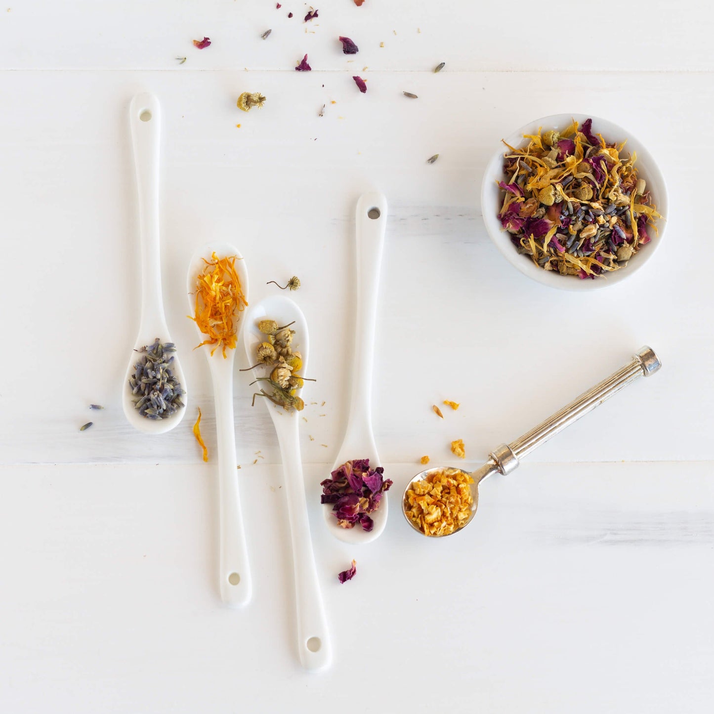 Lavender Lullaby Herbal Tea shown as loose leaf tea in a white bowl next to different spoons full of ingredients.