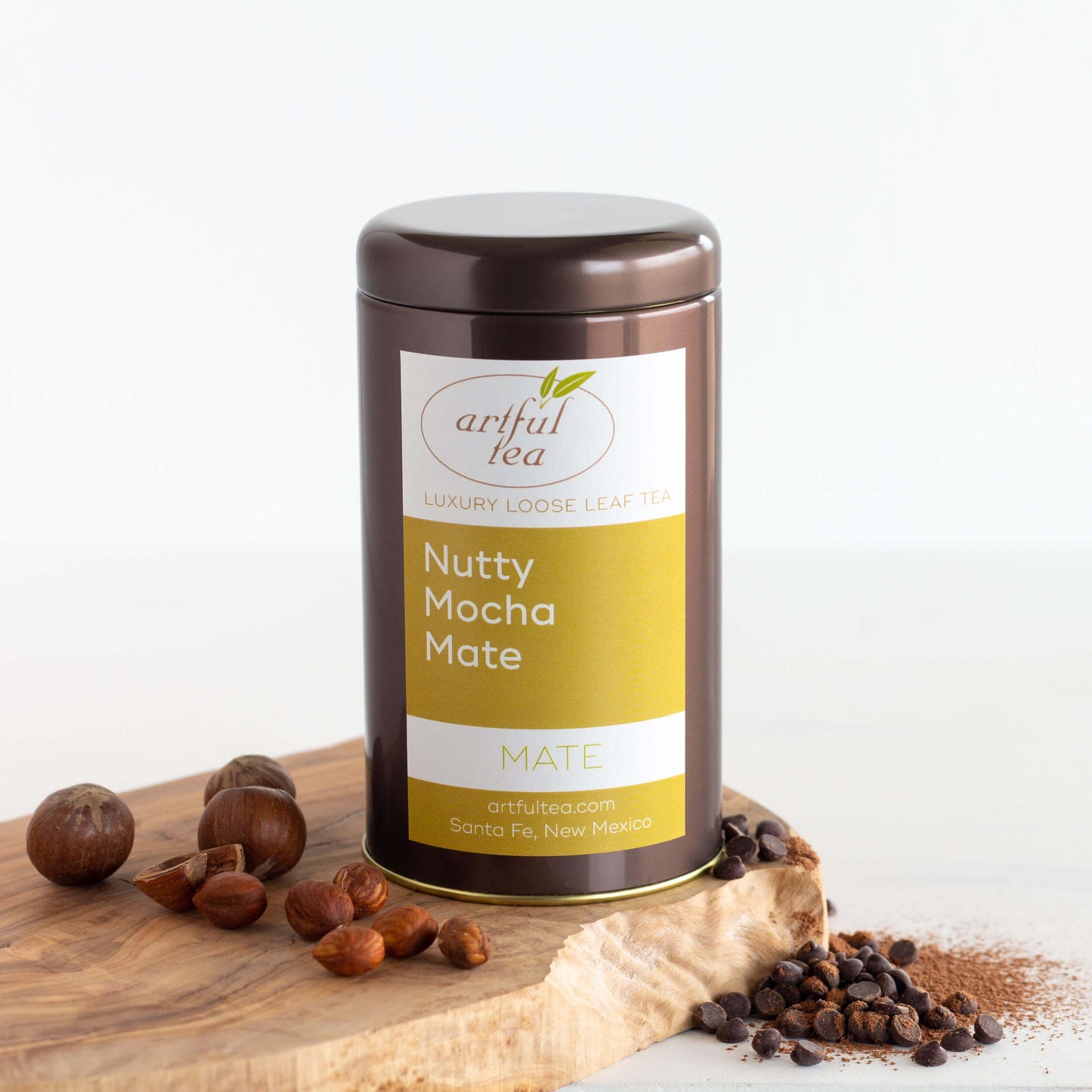 Nutty Mocha Mate Tea shown packaged in a brown tin on top of a wooden plank with ingredients surrounding it.