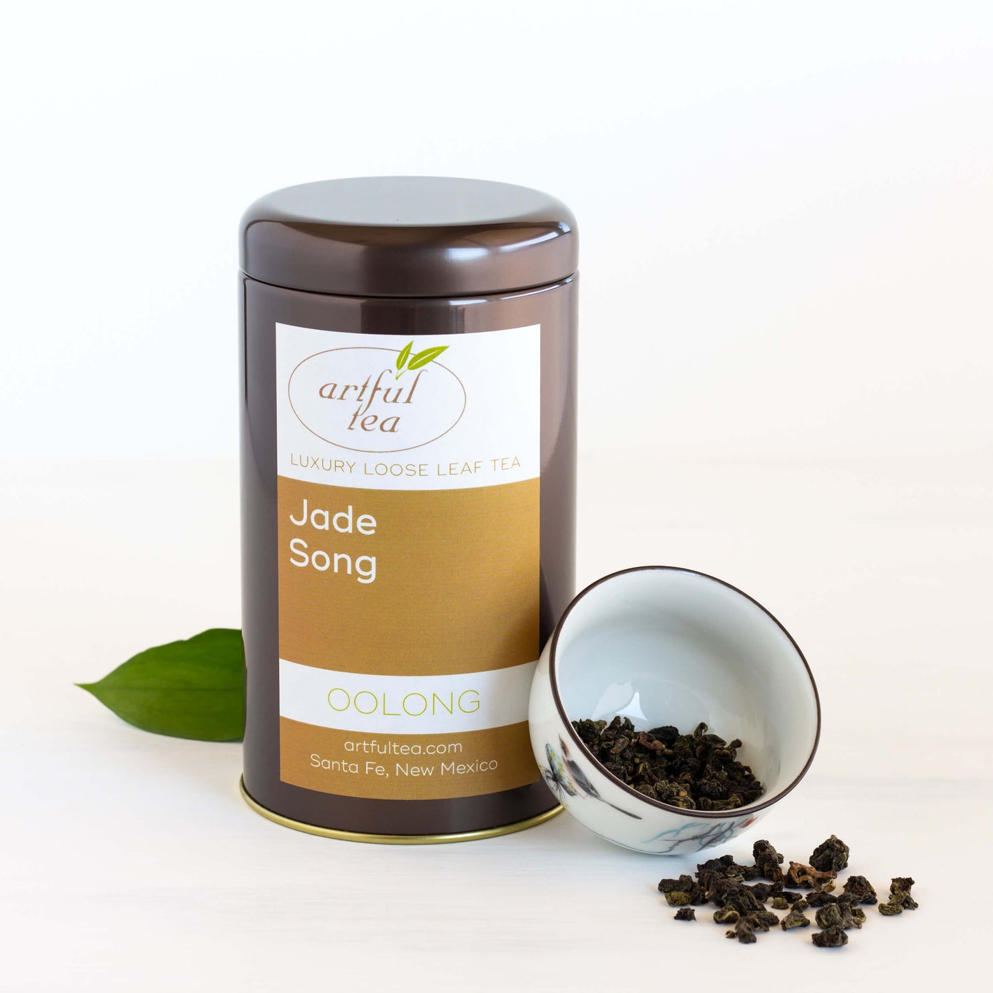 Jade Song Oolong Tea shown packaged in a brown tin with a white bowl of loose leaf tea next to it.