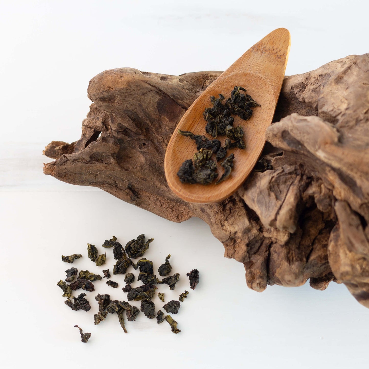 Milk Oolong Tea shown as loose leaf tea on a wooden spoon which is on top of a piece of wood with loose leaf tea sprinkled around nearby.