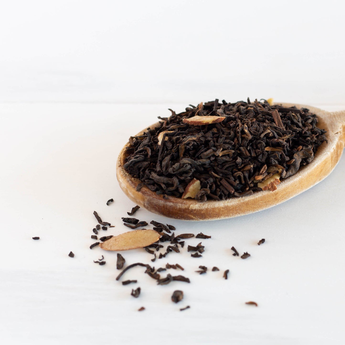 Caramel Pu-erh Tea shown as loose tea leaves spilling out of a wooden spoon.