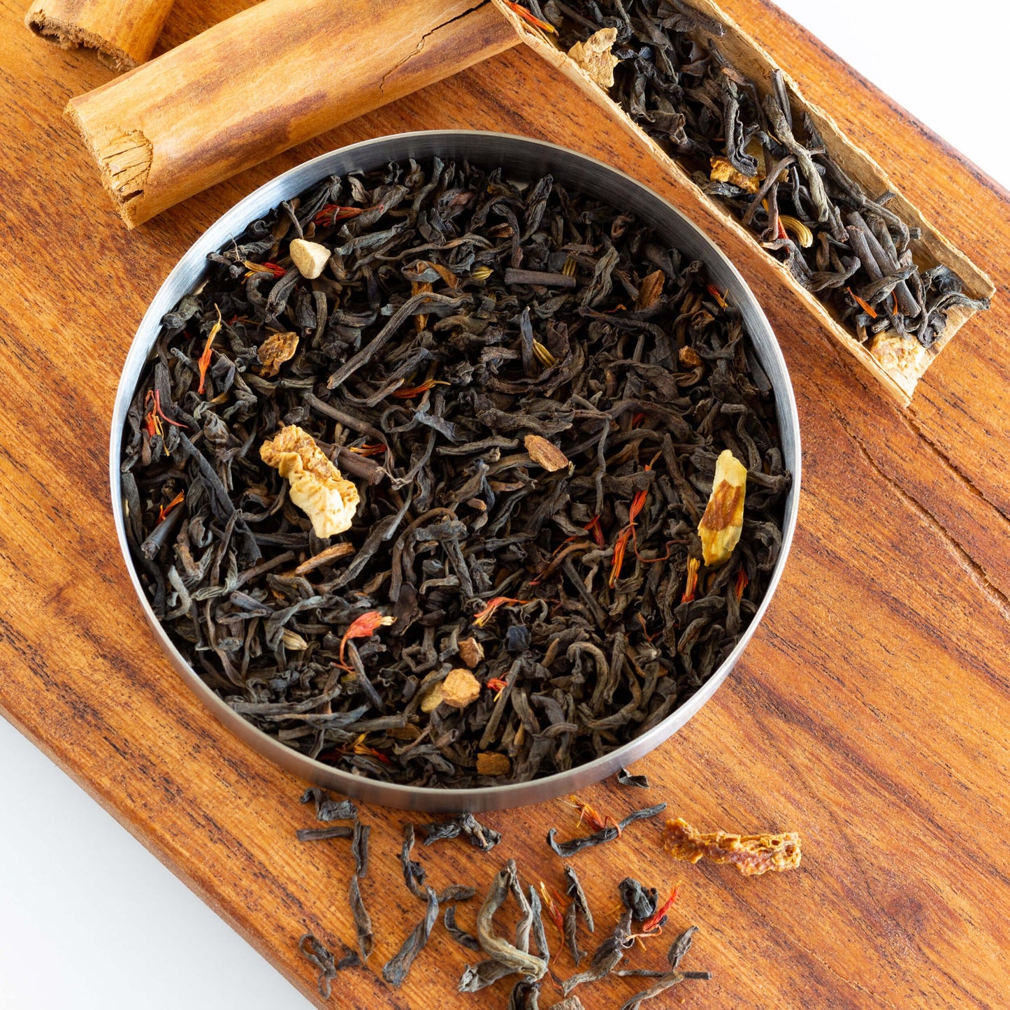 Cinnamon Pu-erh Tea shown as loose leaf tea in a gray bowl on top of a wooden plank with wooden pieces nearby.