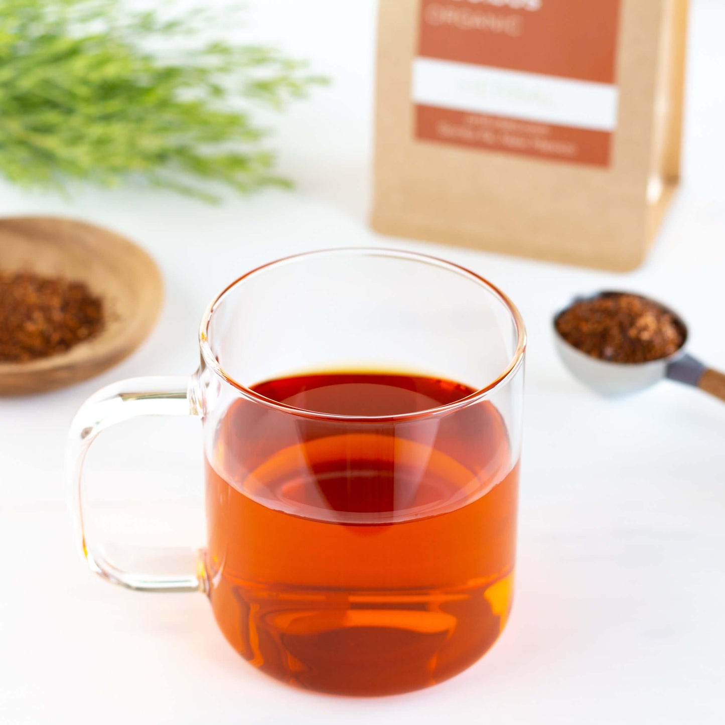 Earl Grey Rooibos Herbal Tea shown brewed in a clear mug near a scoop and bowl of loose leaf tea.
