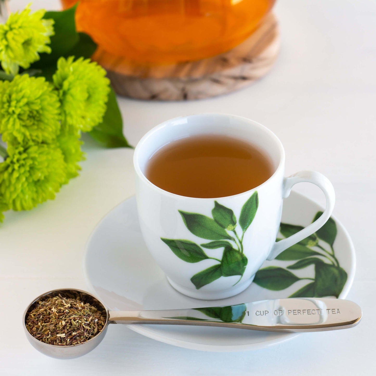 Green Rooibos Herbal Tea shown as brewed tea in a white and green mug with a teaspoon full of loose tea leaves.