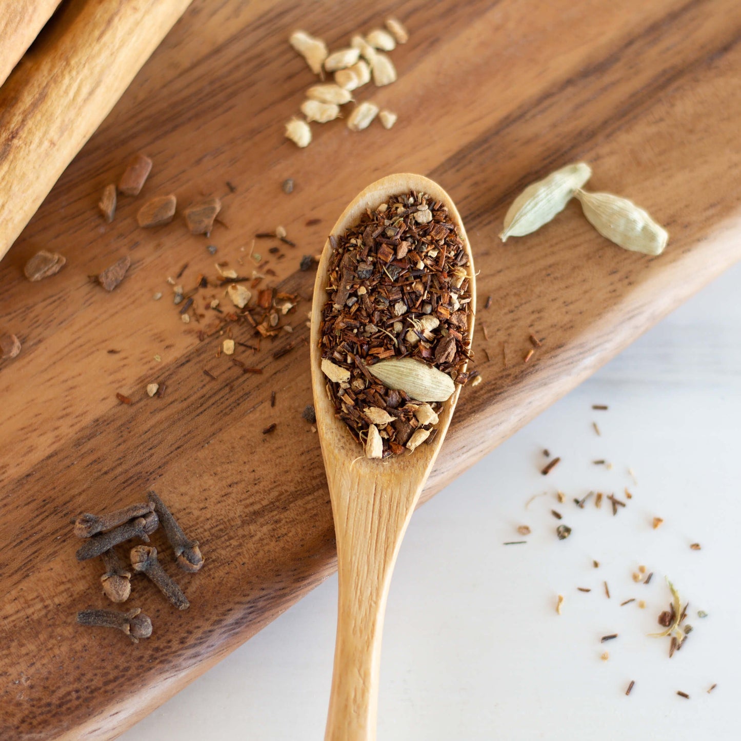 Rooibos Chai Herbal Tea shown from above as loose leaf tea in a wooden spoon with ingredients surrounding it.