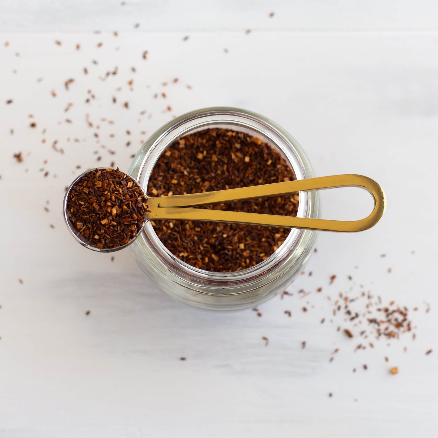 Rooibos Herbal Tea shown from above as loose leaf tea in a jar with a scoop of tea on top.