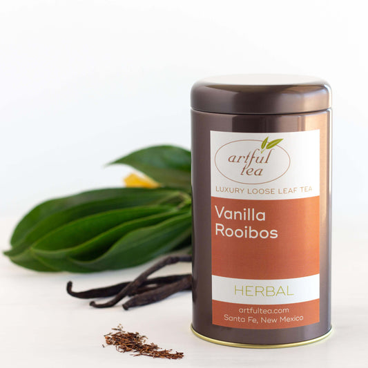 Vanilla Rooibos Herbal Tea shown packaged in a brown tin next to vanilla beans and a plant.